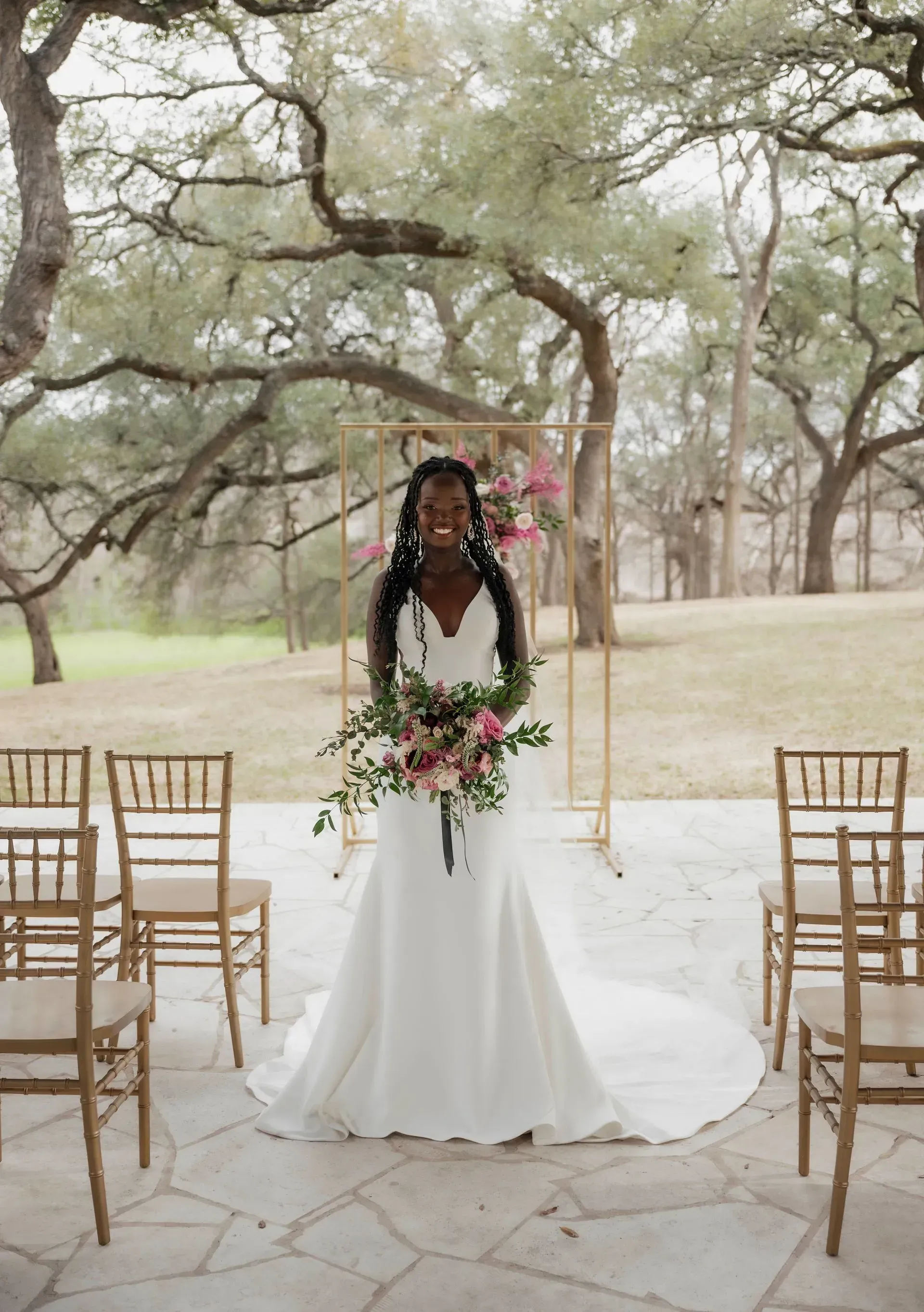 A bride in a white dress is standing in front of a row of chairs holding a bouquet of flowers.