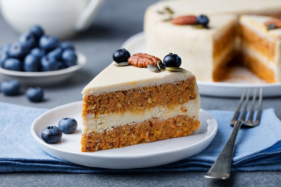 A slice of carrot cake with blueberries on a plate with a fork.
