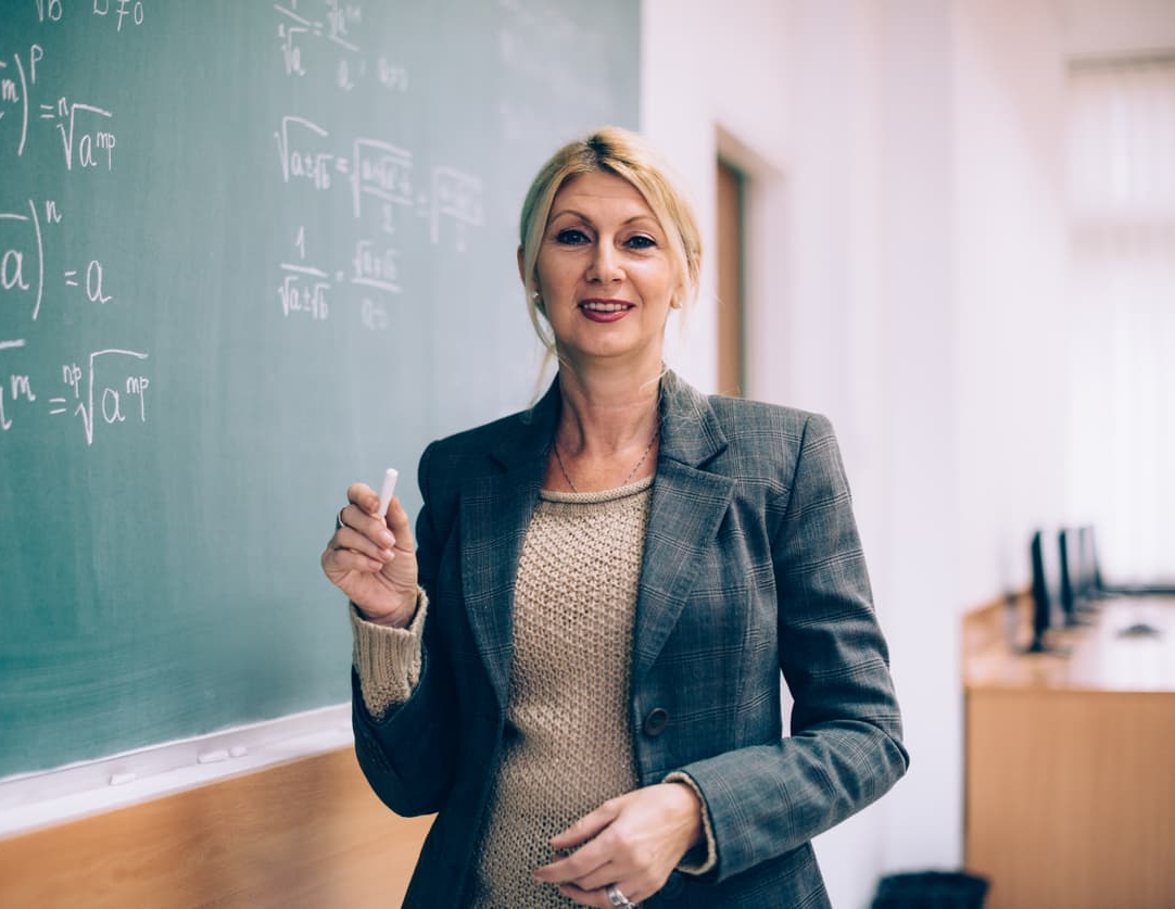 A professor holding chalk stands in front of a chalkboard