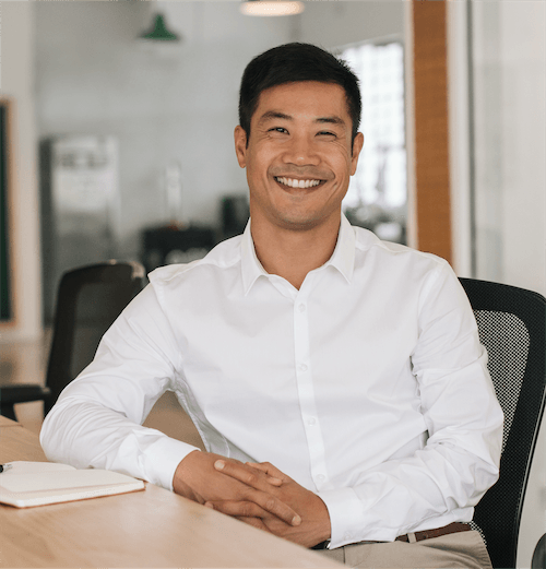 A smiling businessman sitting at a desk with his elbow resting on the table