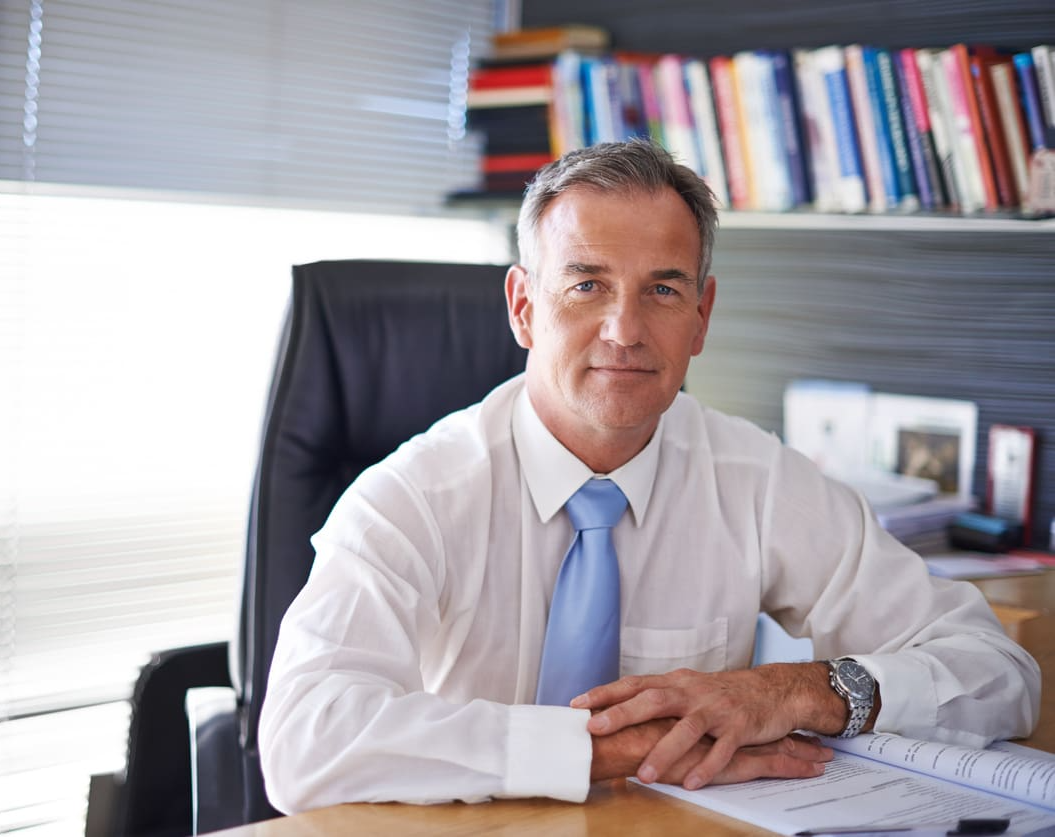 A man in a blue tie and white shirt sits at his desk