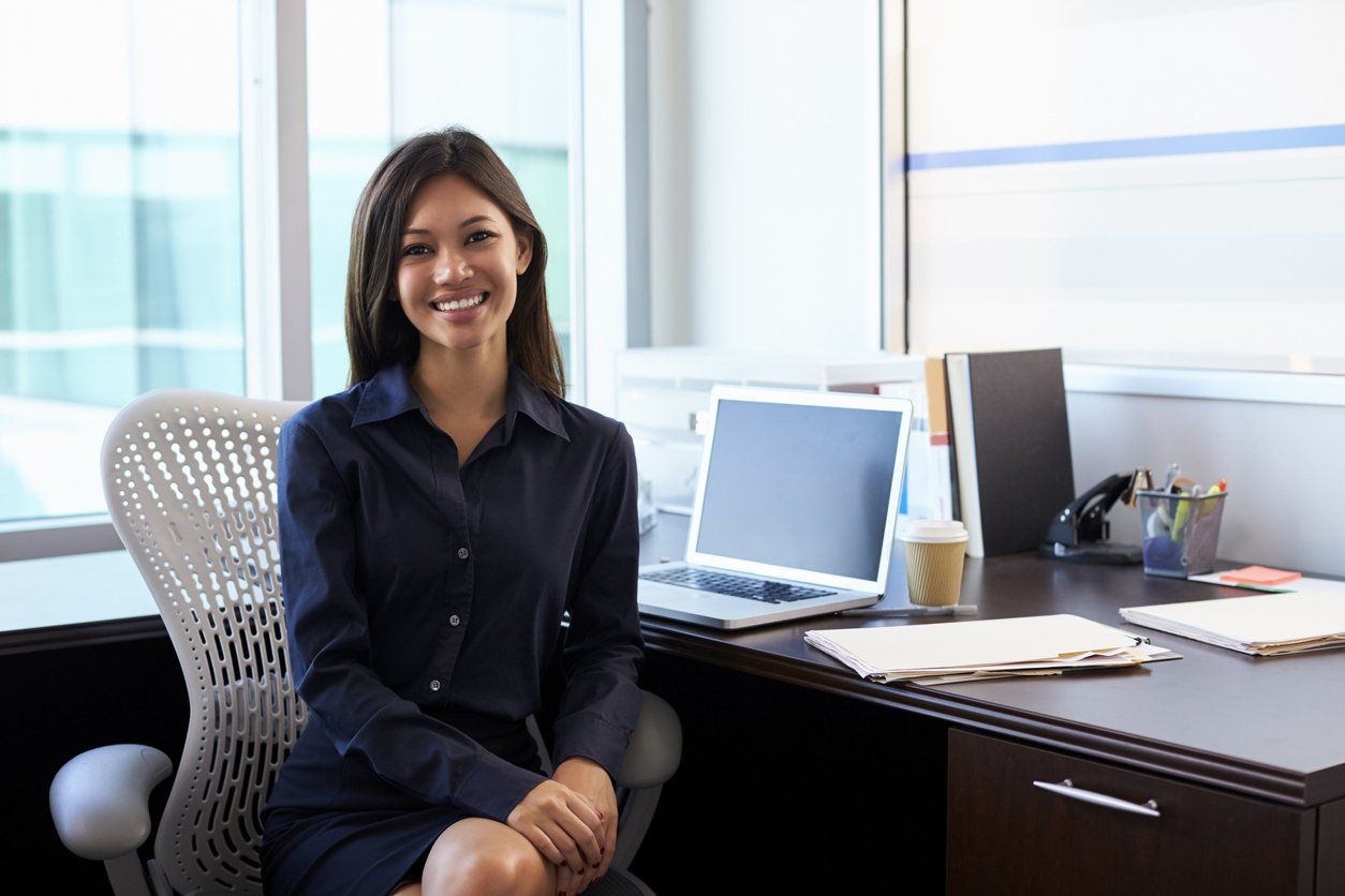 A smiling woman in front of her desk and laptop