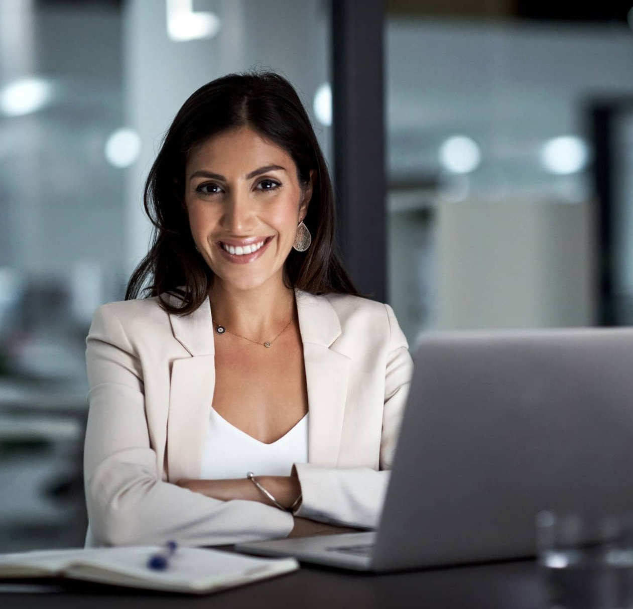 A businesswoman smiles and is seated at a table with her laptop and notepad