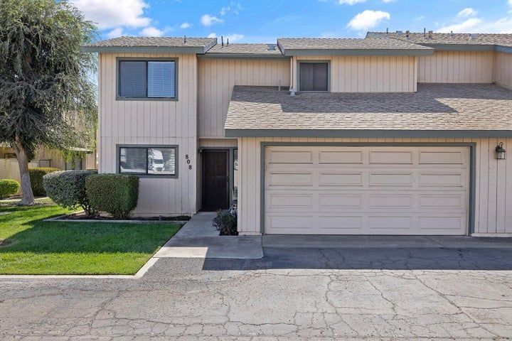 Beige two-story townhouse with a two-car garage, blue windows, and a front lawn.