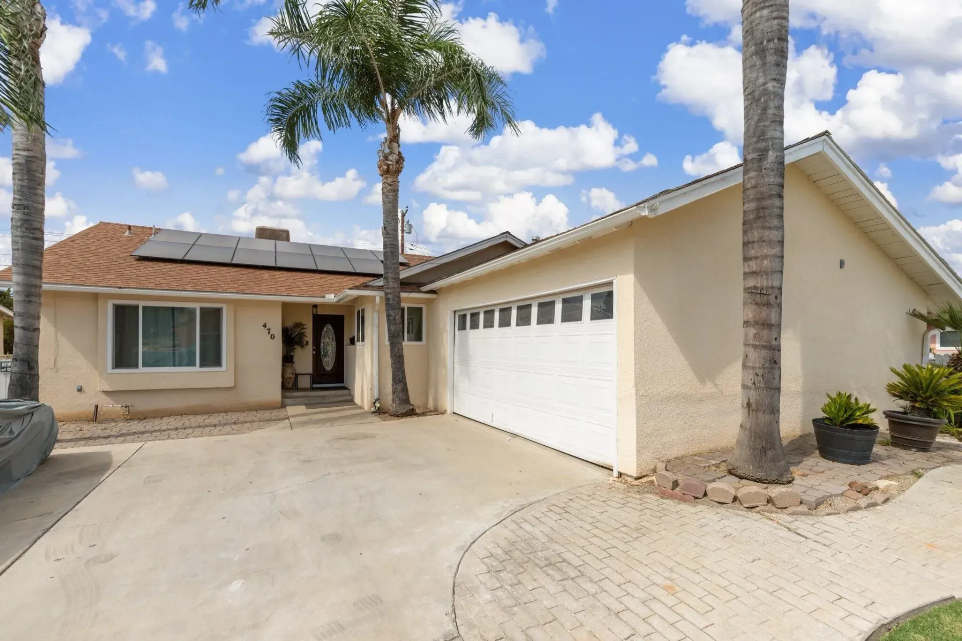 Beige single-story house with palm trees, driveway, and white garage door under a blue sky.