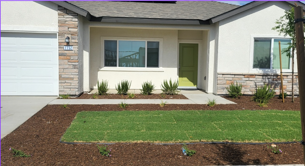 A single-story house with a green door and manicured lawn.