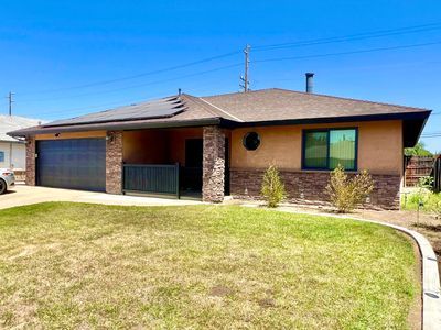 Tan ranch-style house with a garage, brown trim, brick accents, and a green lawn under a blue sky.