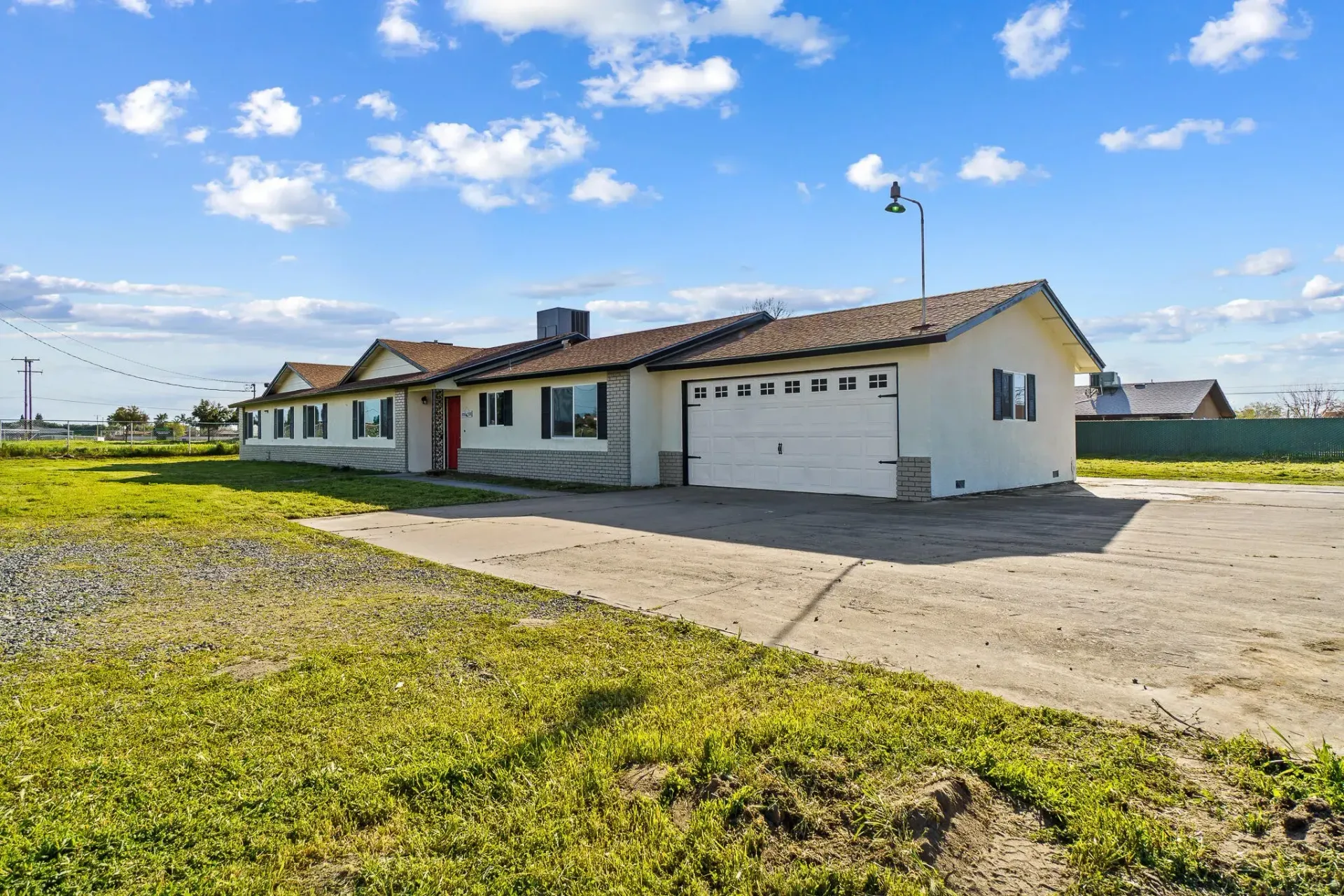 Single-story white house with a gray garage door and red door. Green lawn and blue sky.