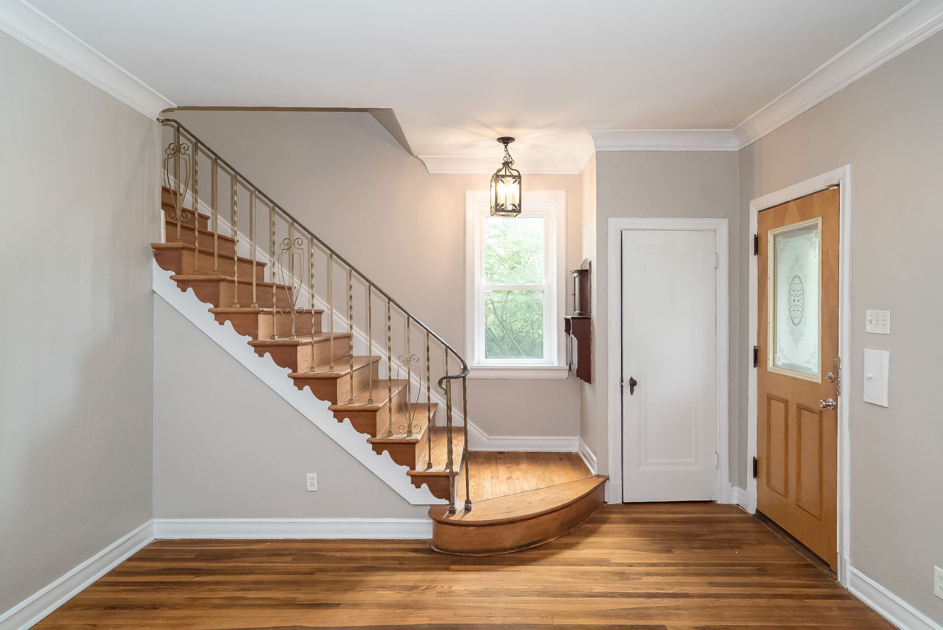 image of an empty living and entry space of a home with a pretty stair case and wooden front door