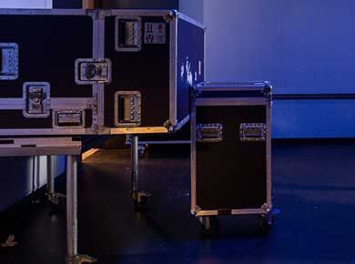 Schwarze Gerätekoffer mit silberfarbenen Beschlägen, einige auf Metallständern, in einem Raum mit blauer Beleuchtung.