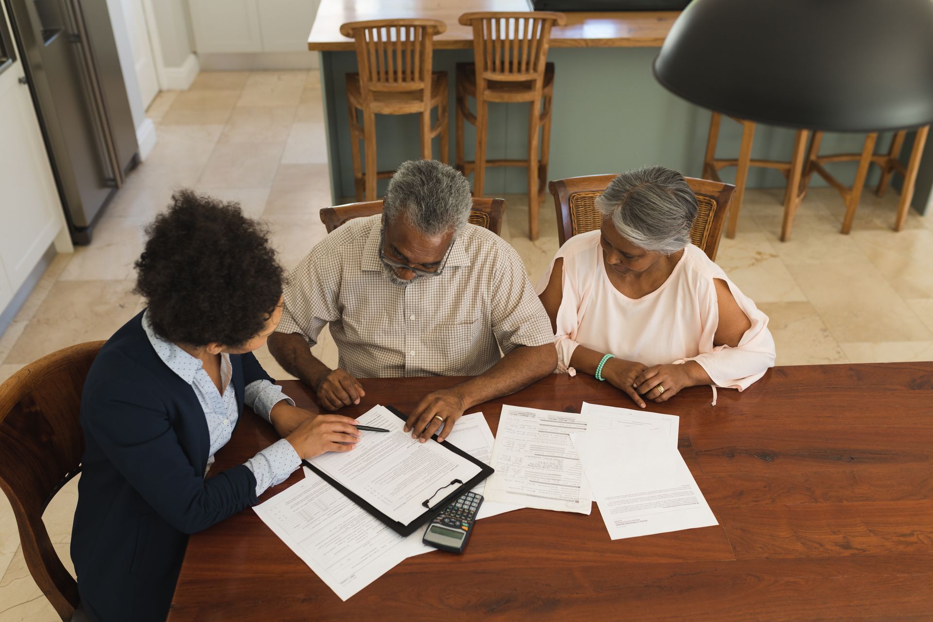 Person showing documents to a couple at a table. Papers and a calculator are visible.