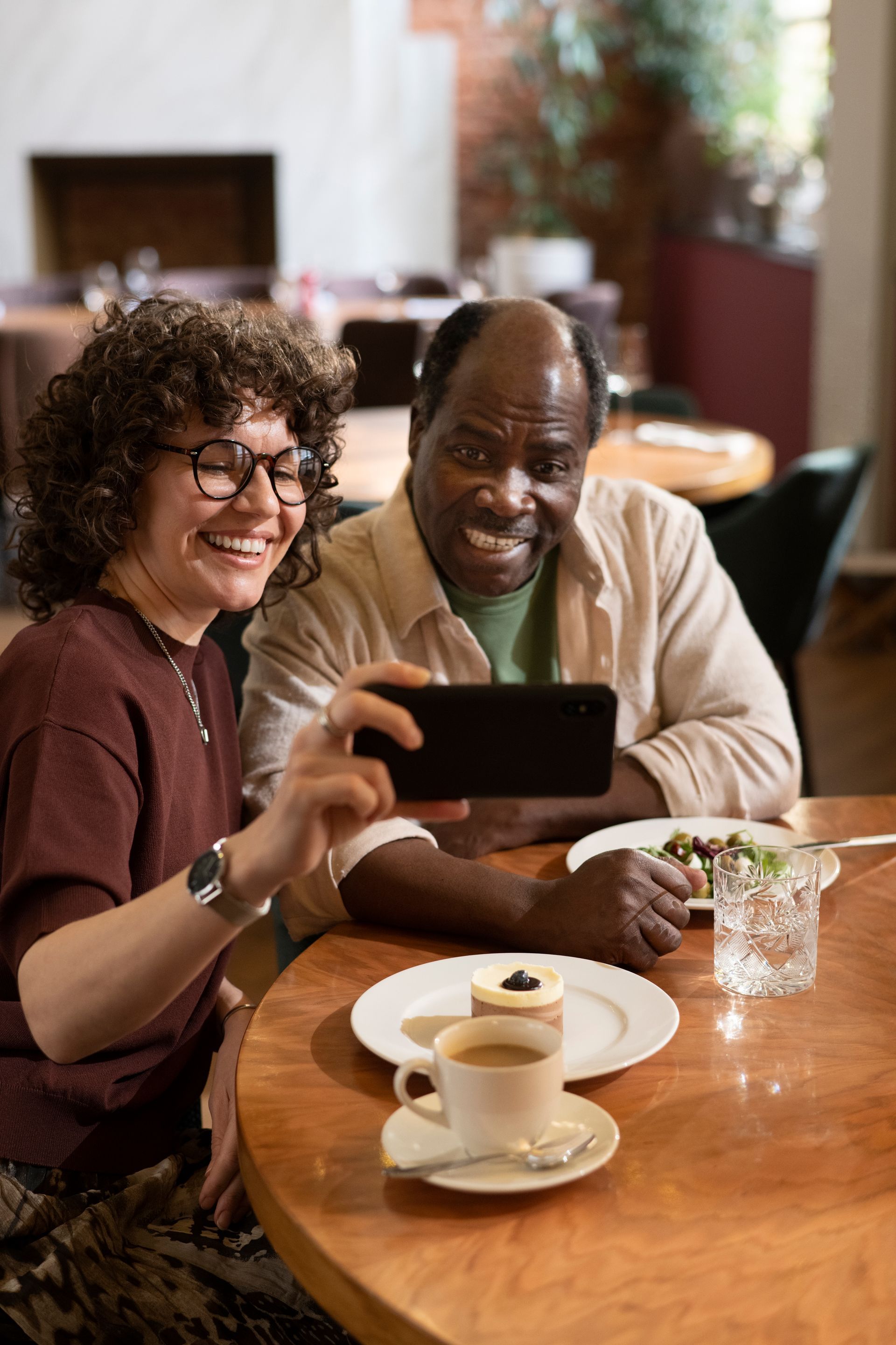 Woman and man at a table in a restaurant, taking a photo of their dessert. They smile.