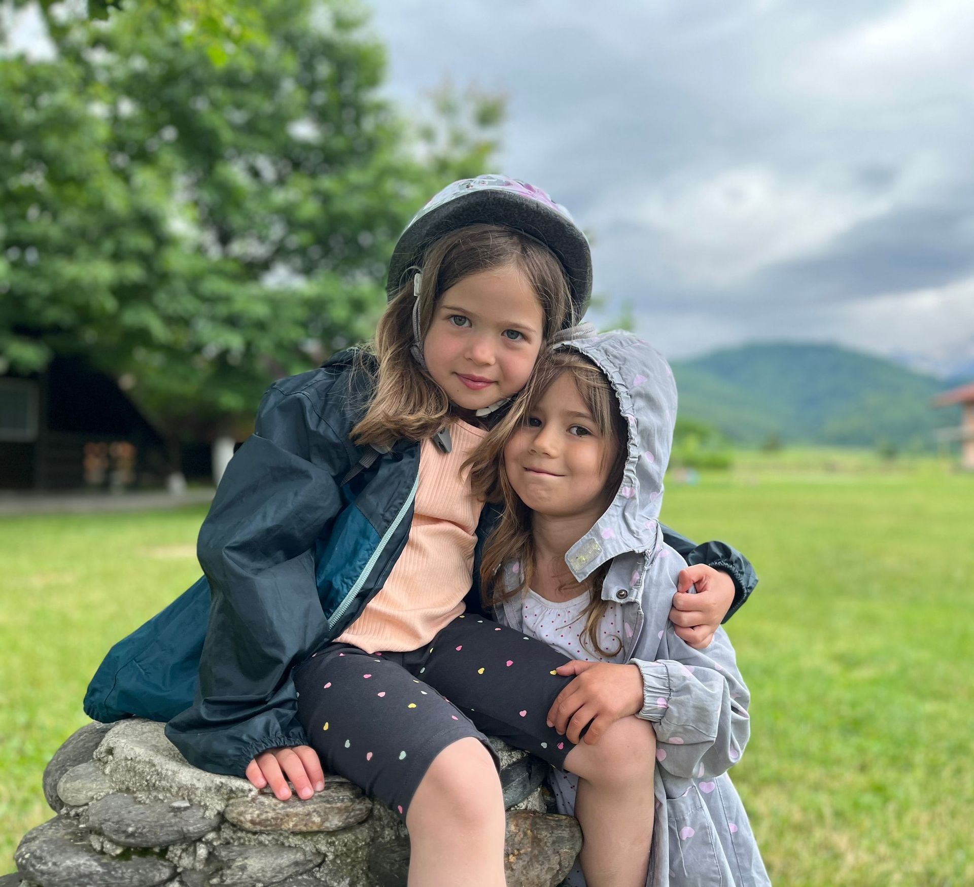 Two little girls are sitting next to each other on a rock.
