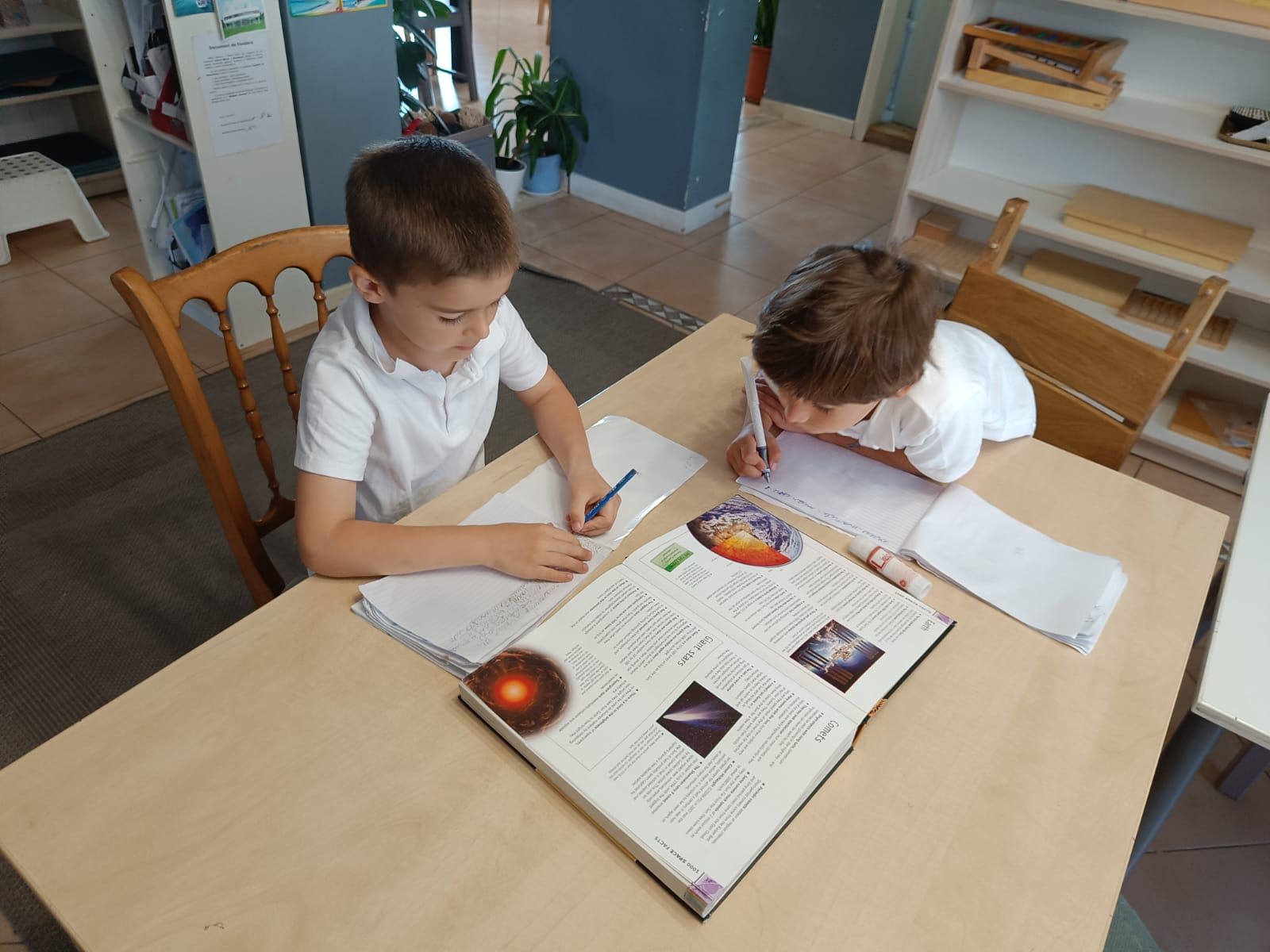 Two young boys are sitting at a table reading a book