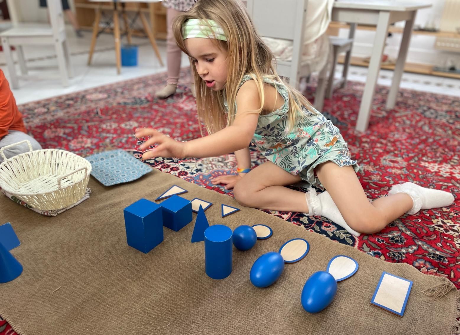 A little girl is sitting on the floor playing with blue geometric shapes.