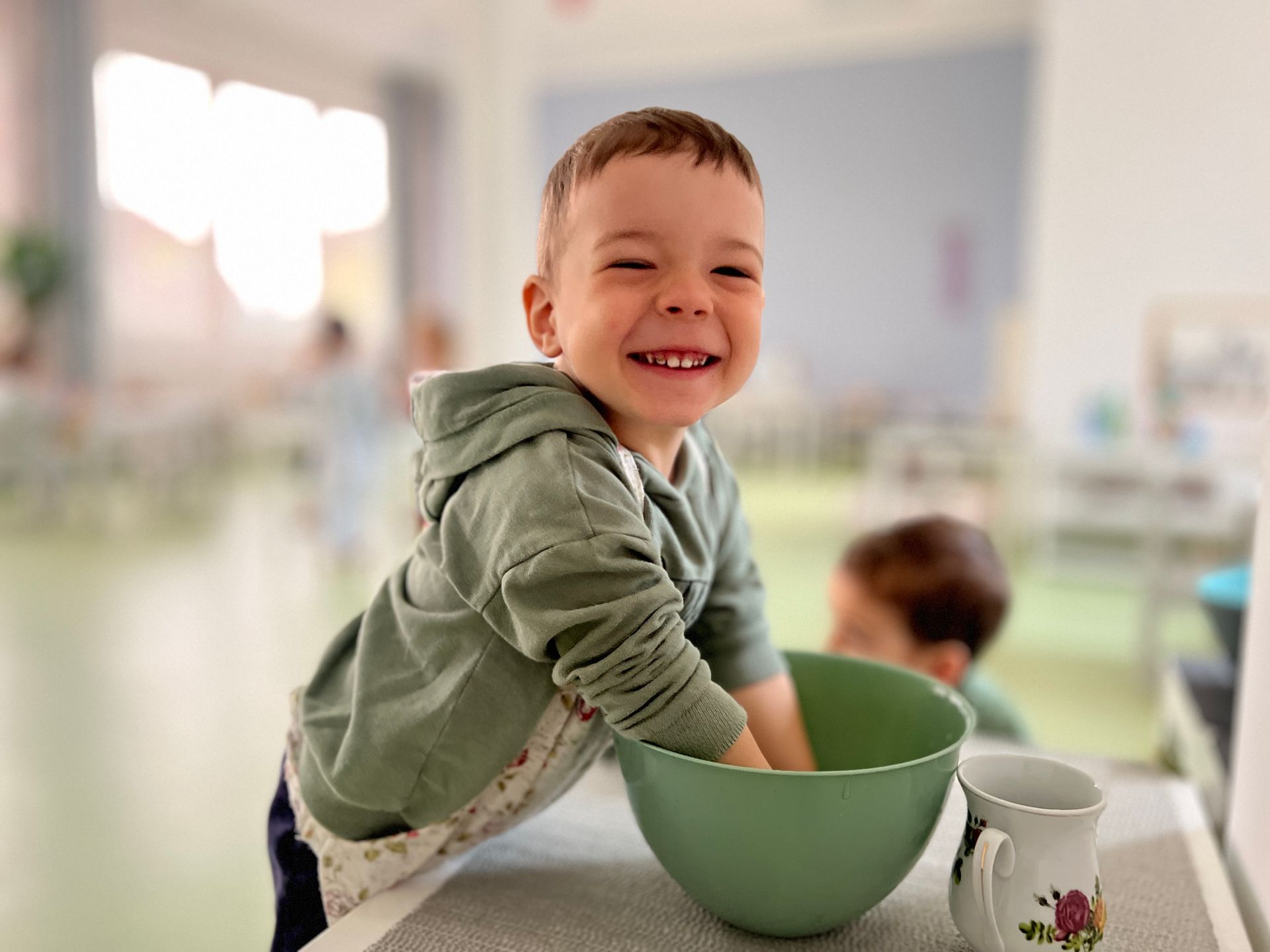 A young boy is playing with a green bowl on a table.