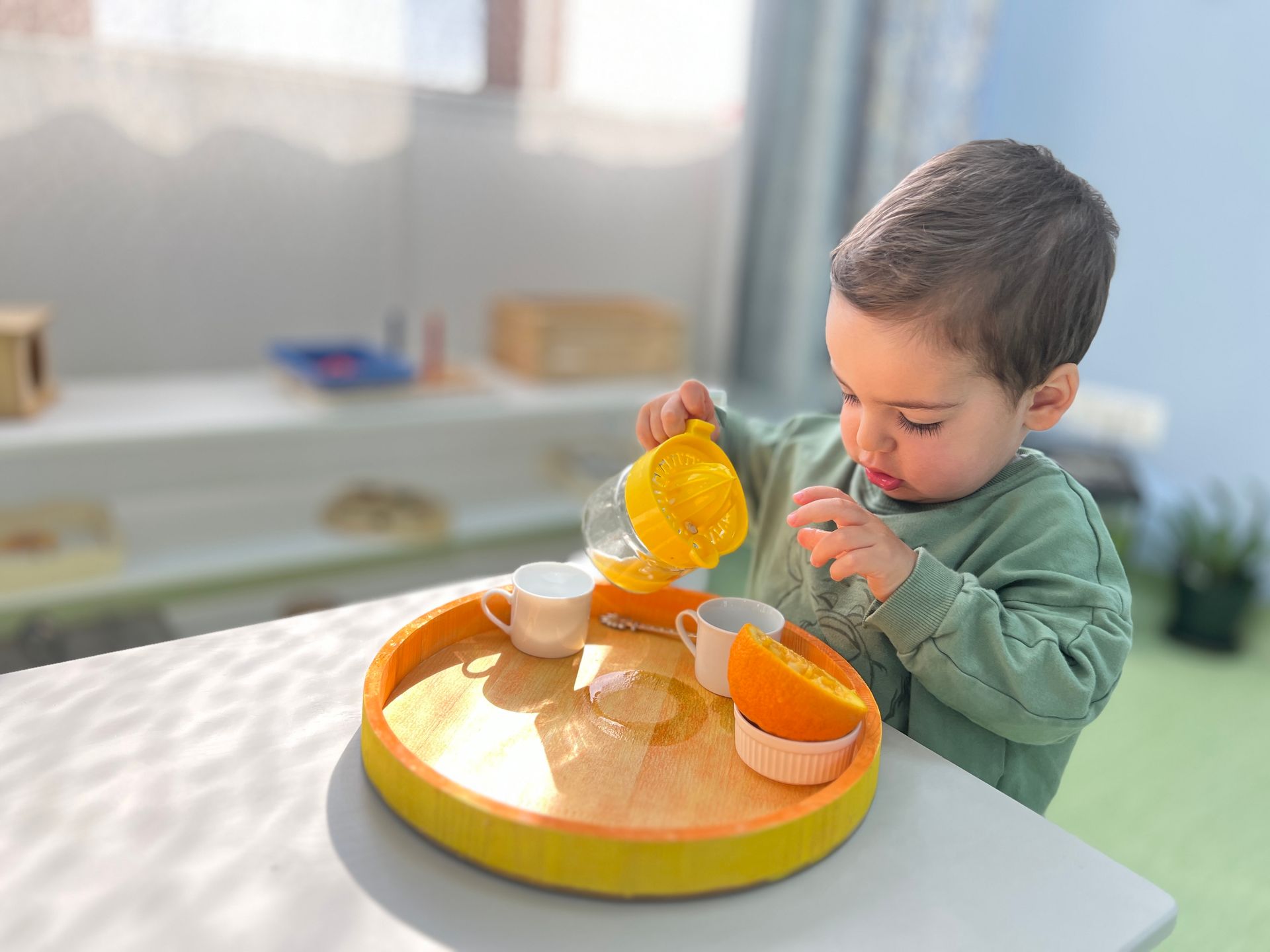 A little boy is playing with a tea set on a table.