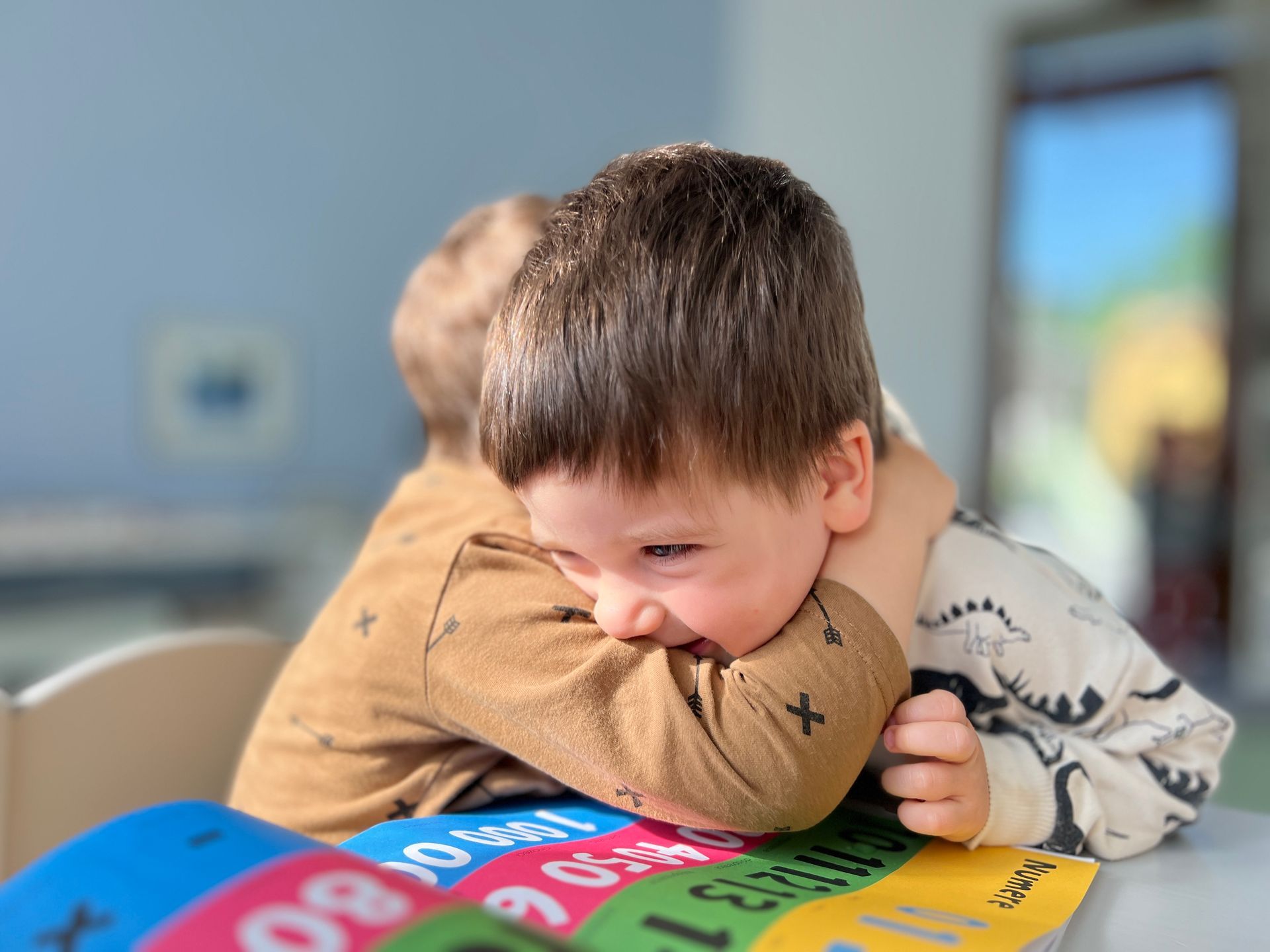 A little boy is hugging another little boy on a table.