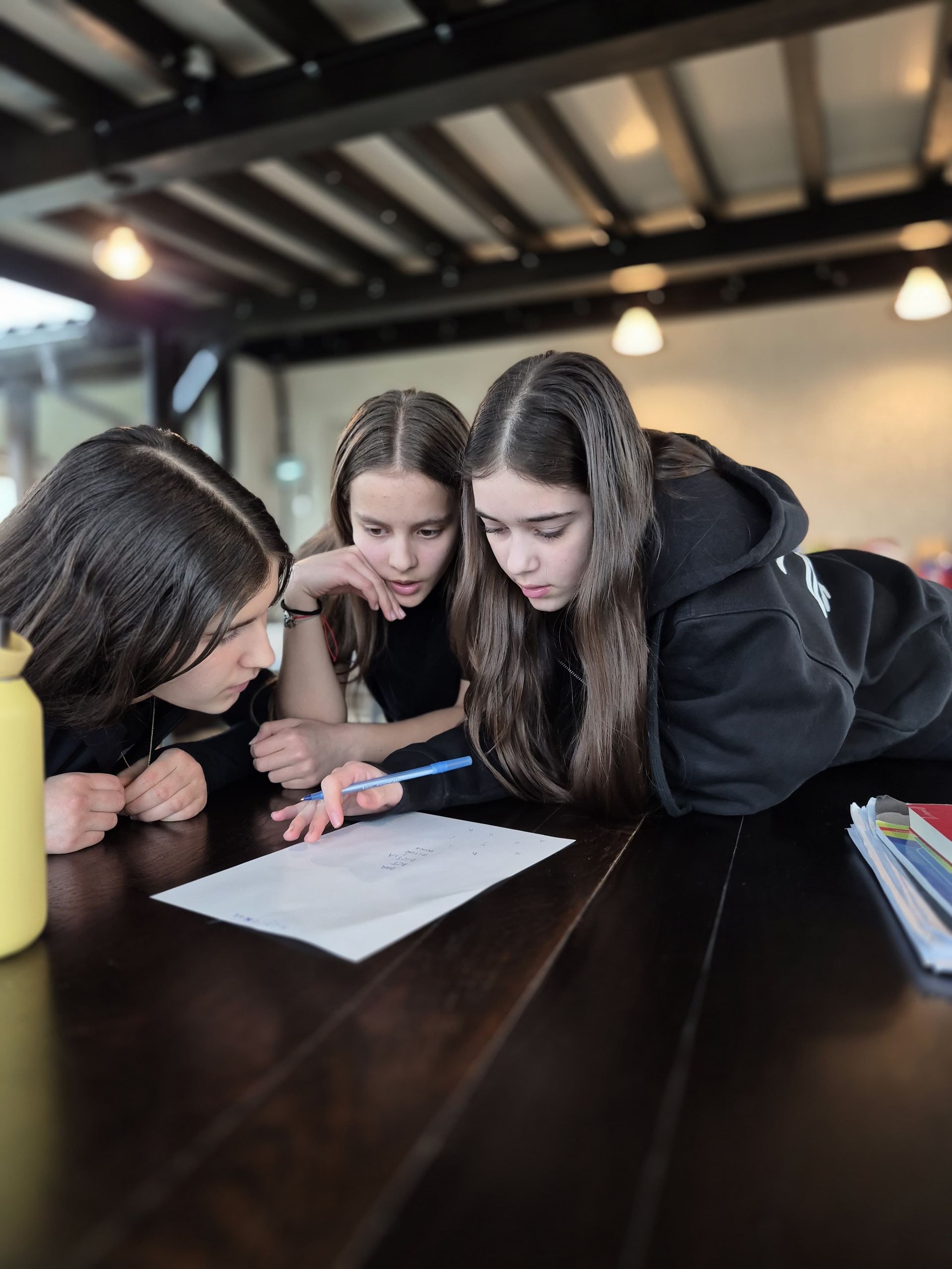 Three girls are looking at a piece of paper on a table.