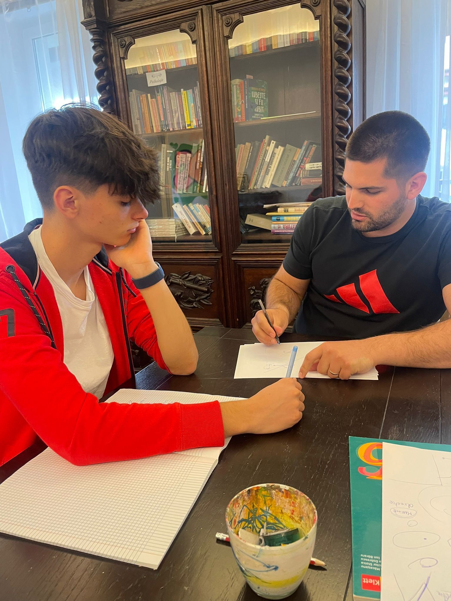 A man is helping a young boy with his homework at a table.