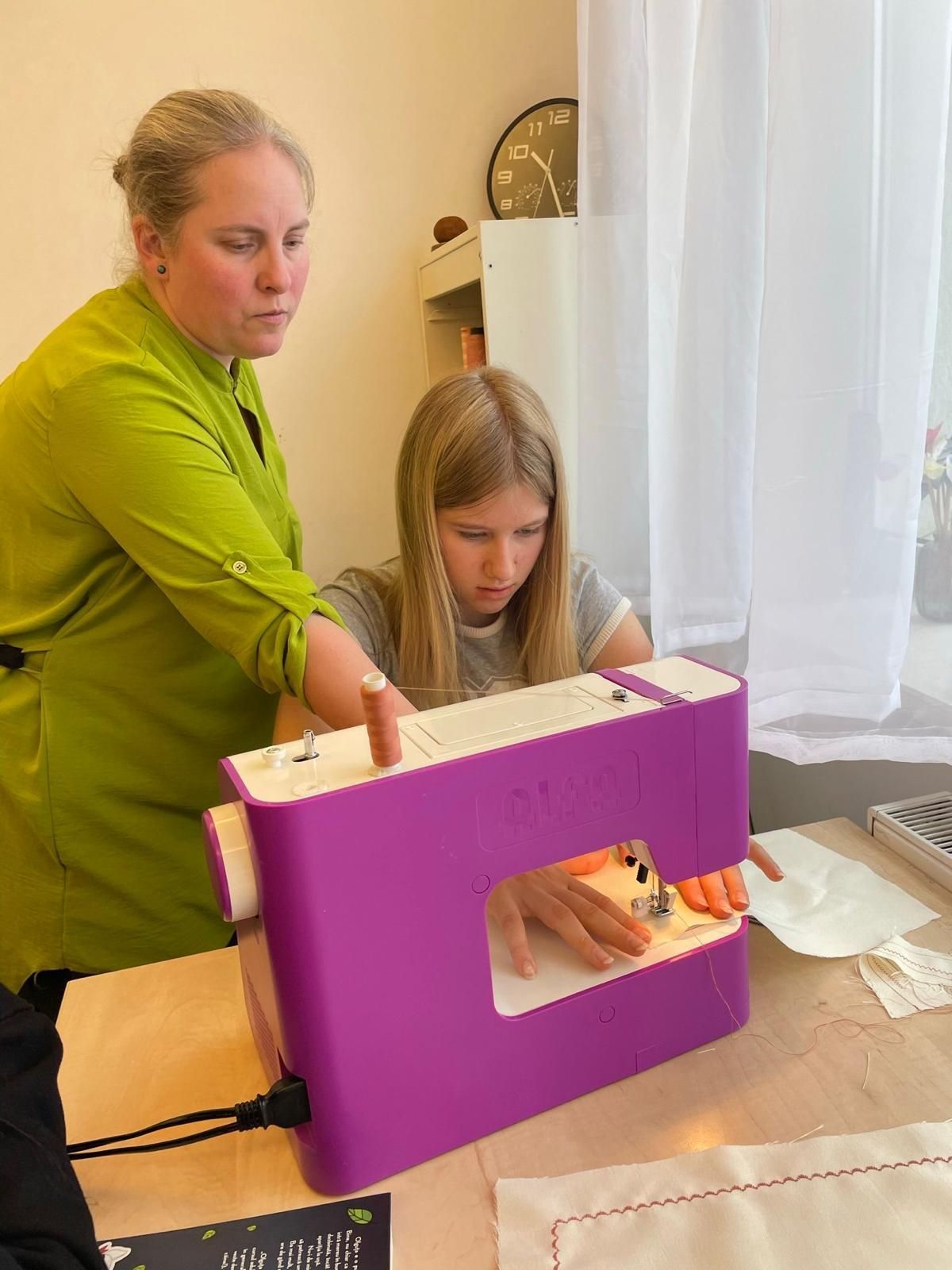 A woman is teaching a young girl how to use a sewing machine.