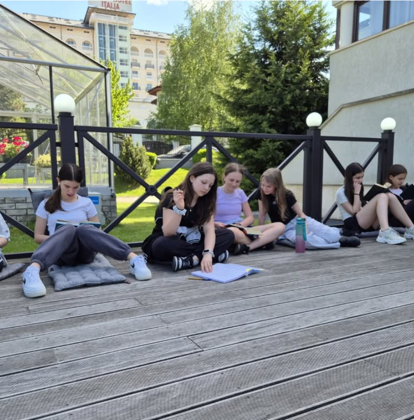 A group of girls sit on a wooden deck reading books