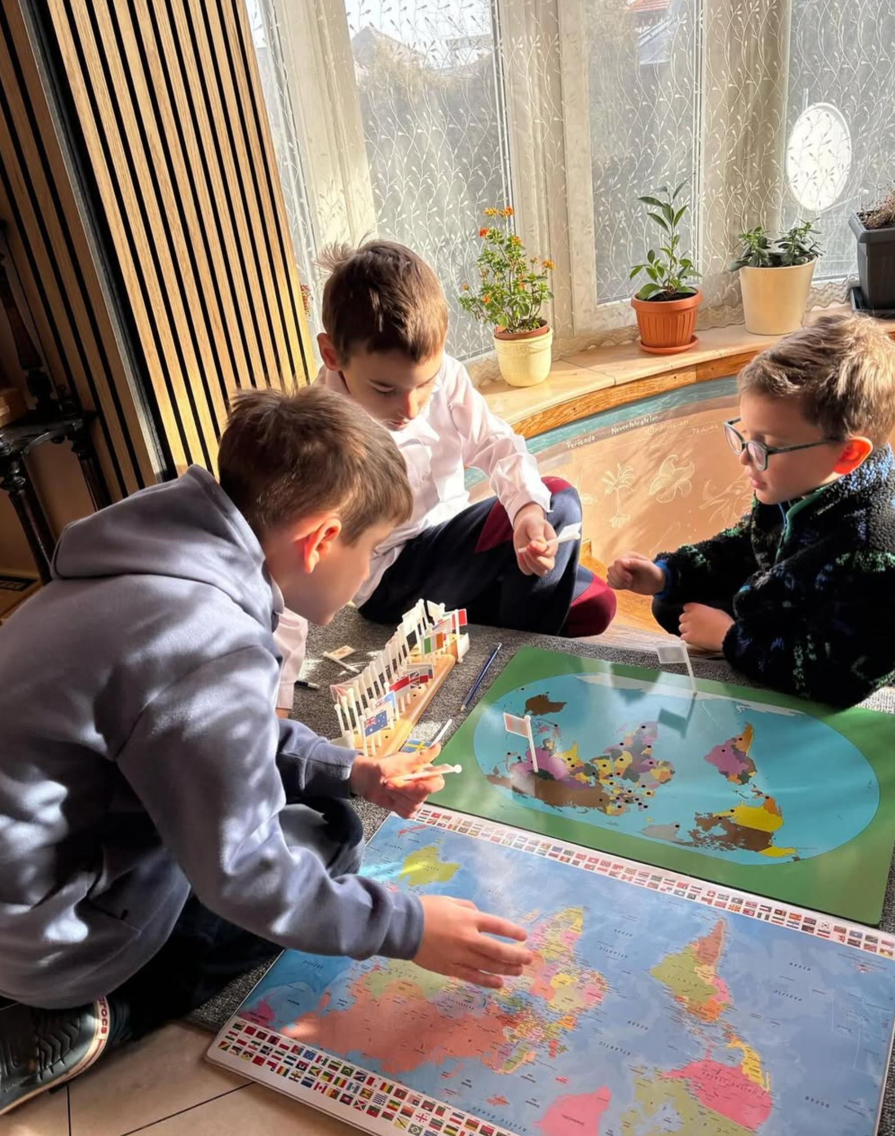 Three young boys are sitting on the floor looking at a map of the world.