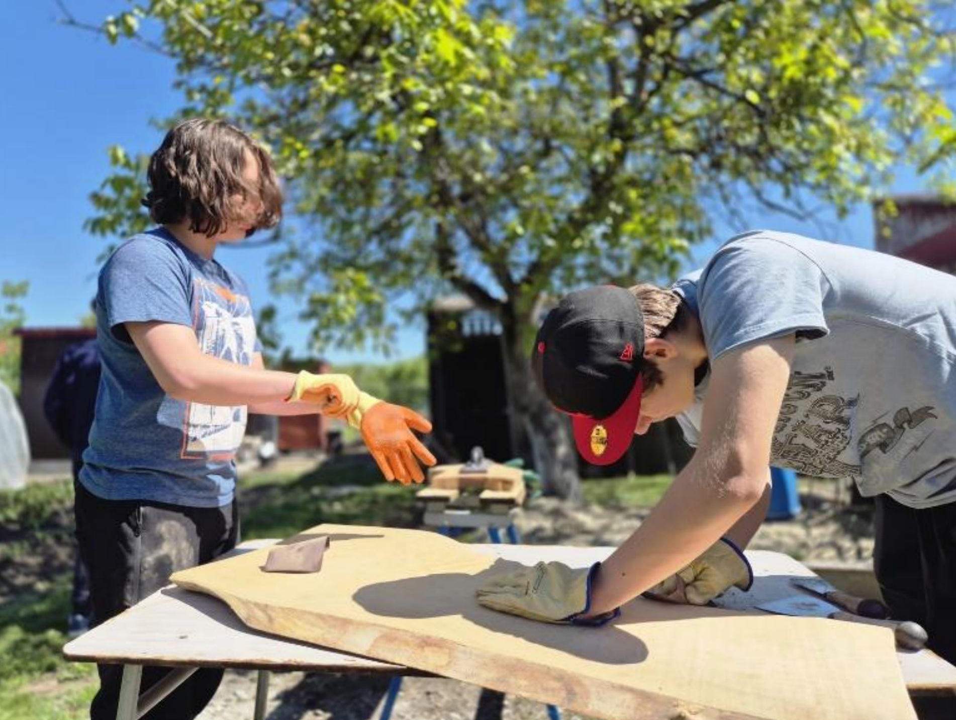 Two men are working on a piece of wood on a table.