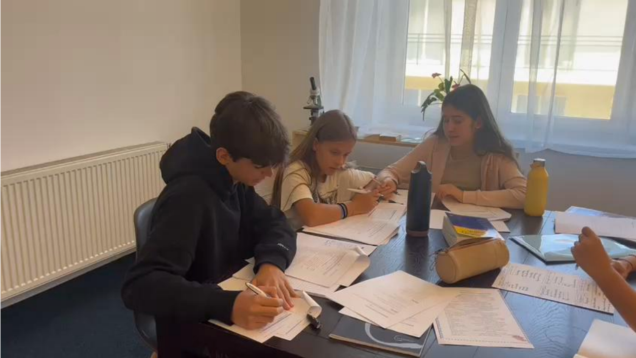 A group of children are sitting at a table writing on papers.