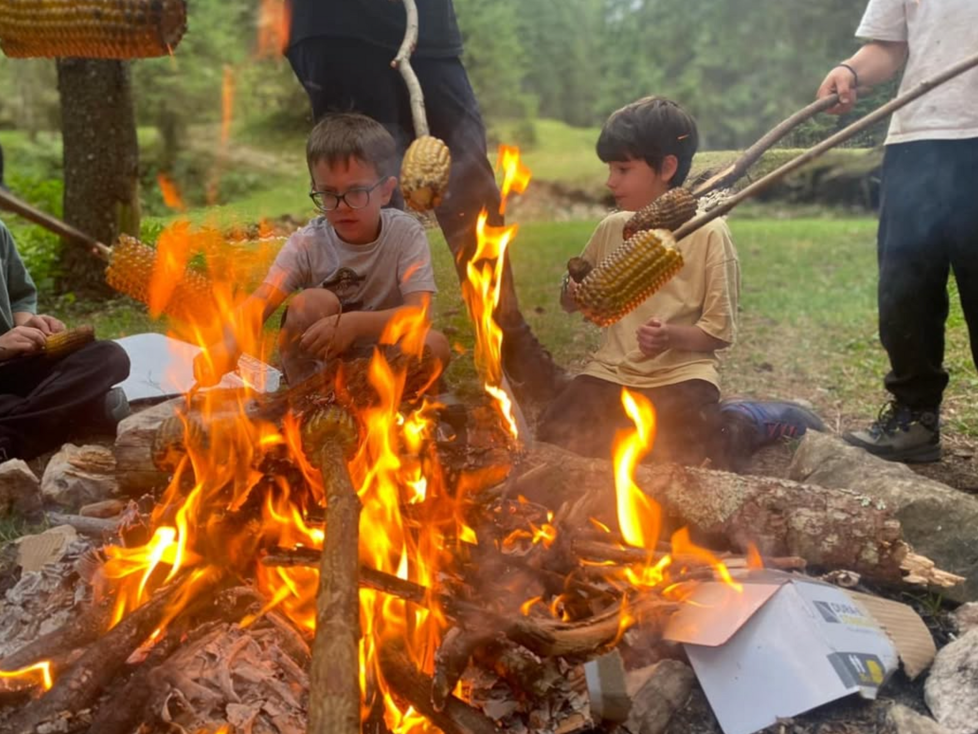 A group of children are sitting around a campfire eating corn on the cob.