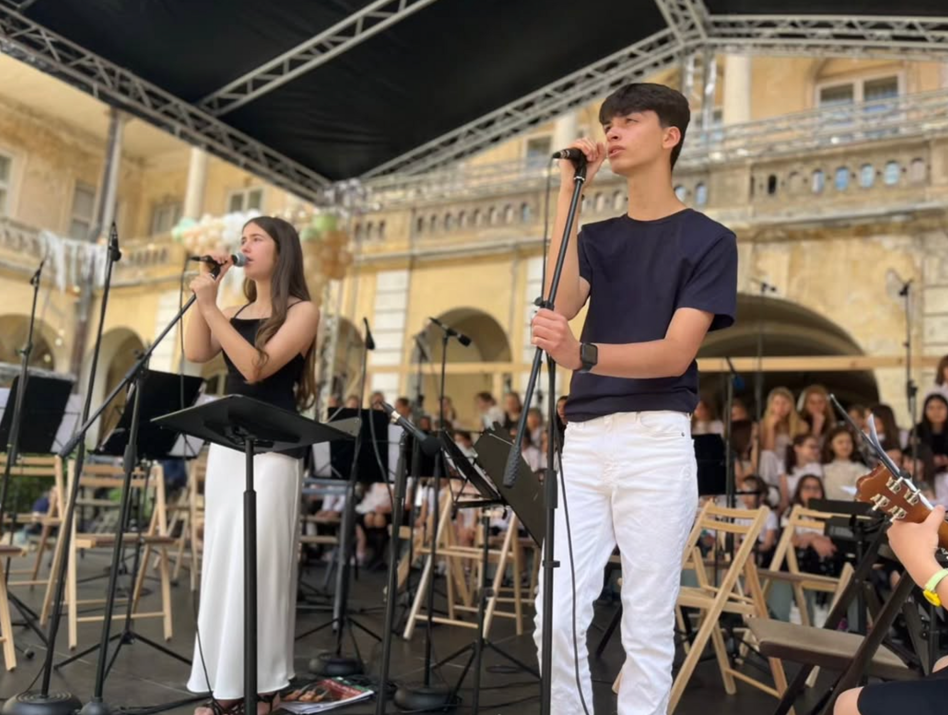 A boy and a girl are singing into microphones on a stage.
