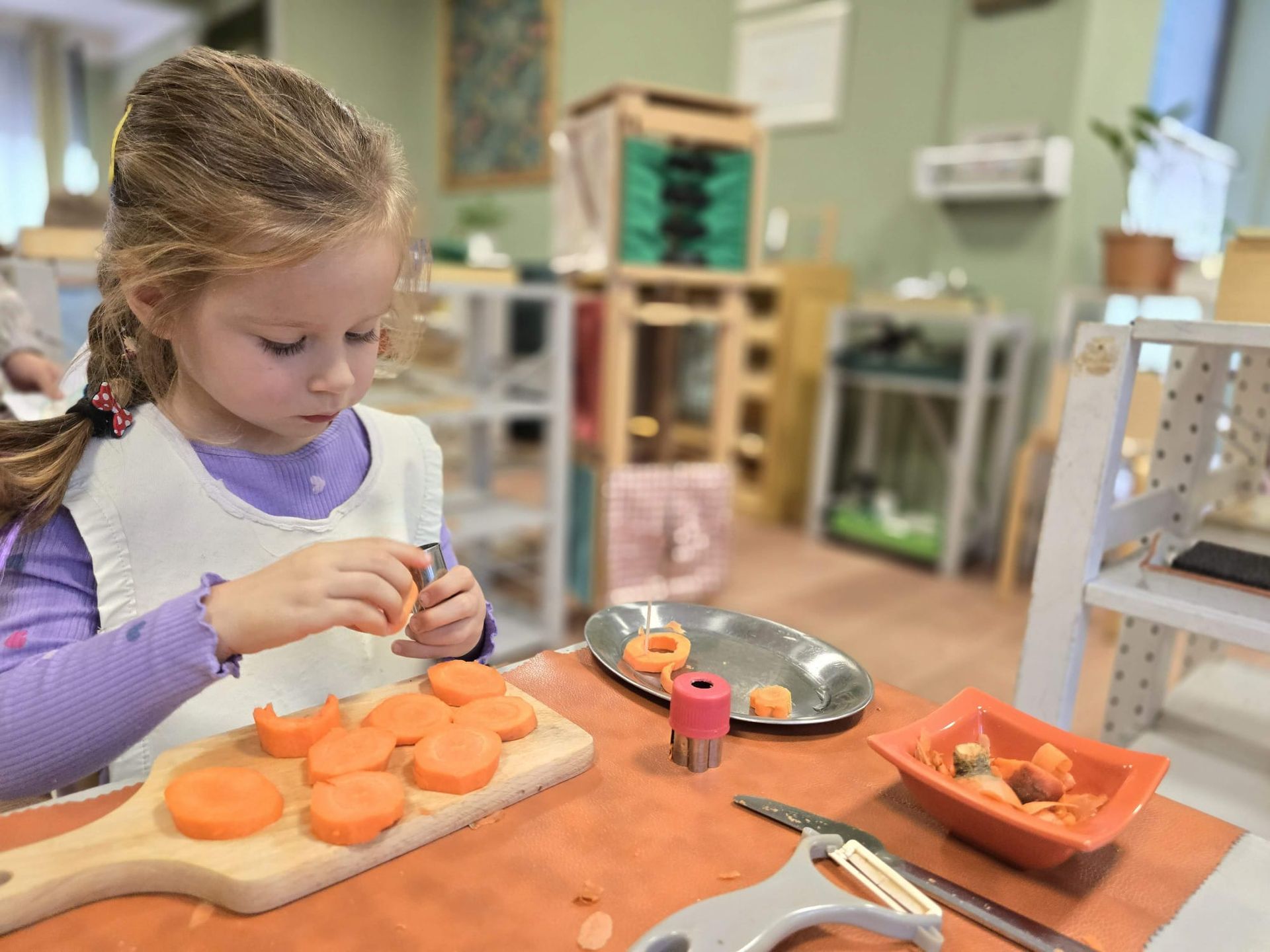 A little girl is cutting carrots on a cutting board.