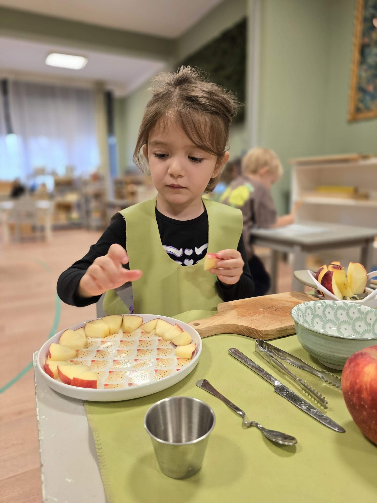 A little girl is sitting at a table eating apples.