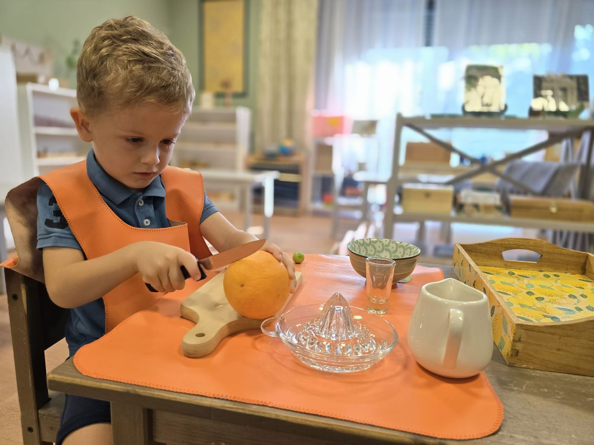 A young boy is sitting at a table cutting an orange.
