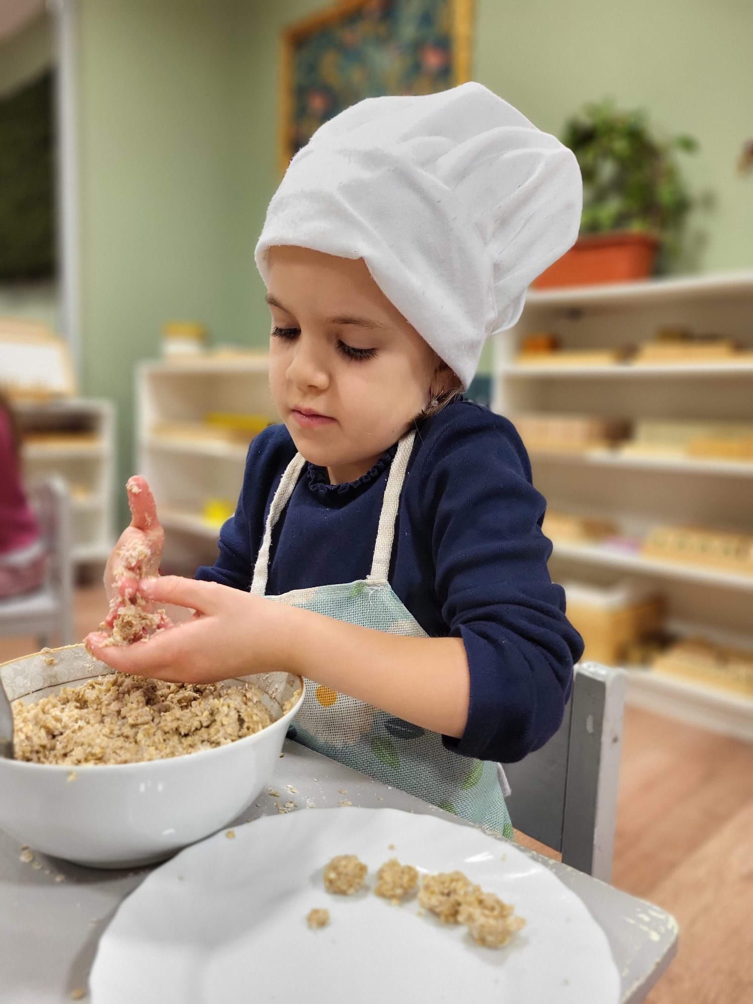 A little boy wearing a chef 's hat and apron is mixing food in a bowl.