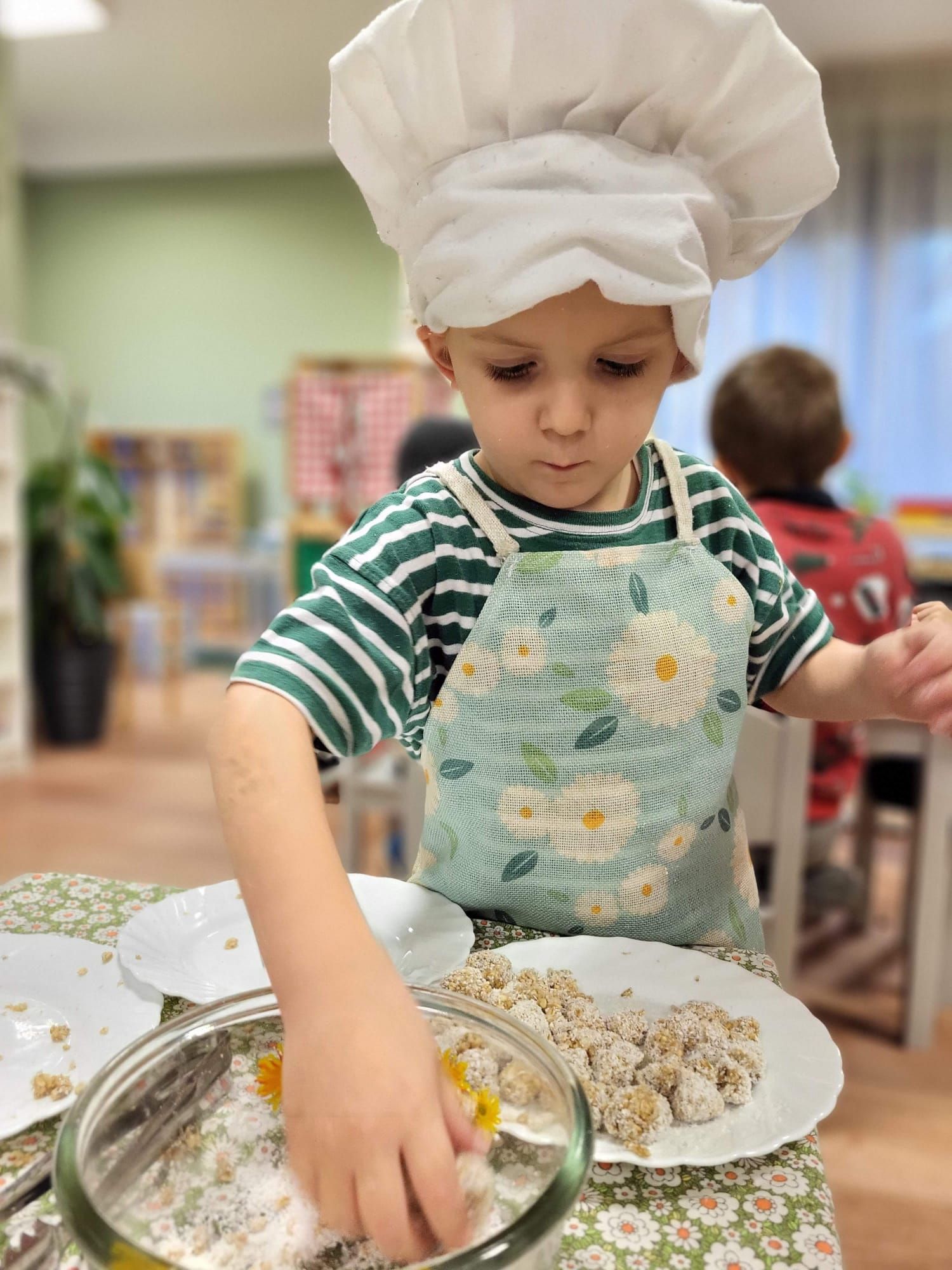 A little boy wearing a chef 's hat and apron is mixing food in a bowl.