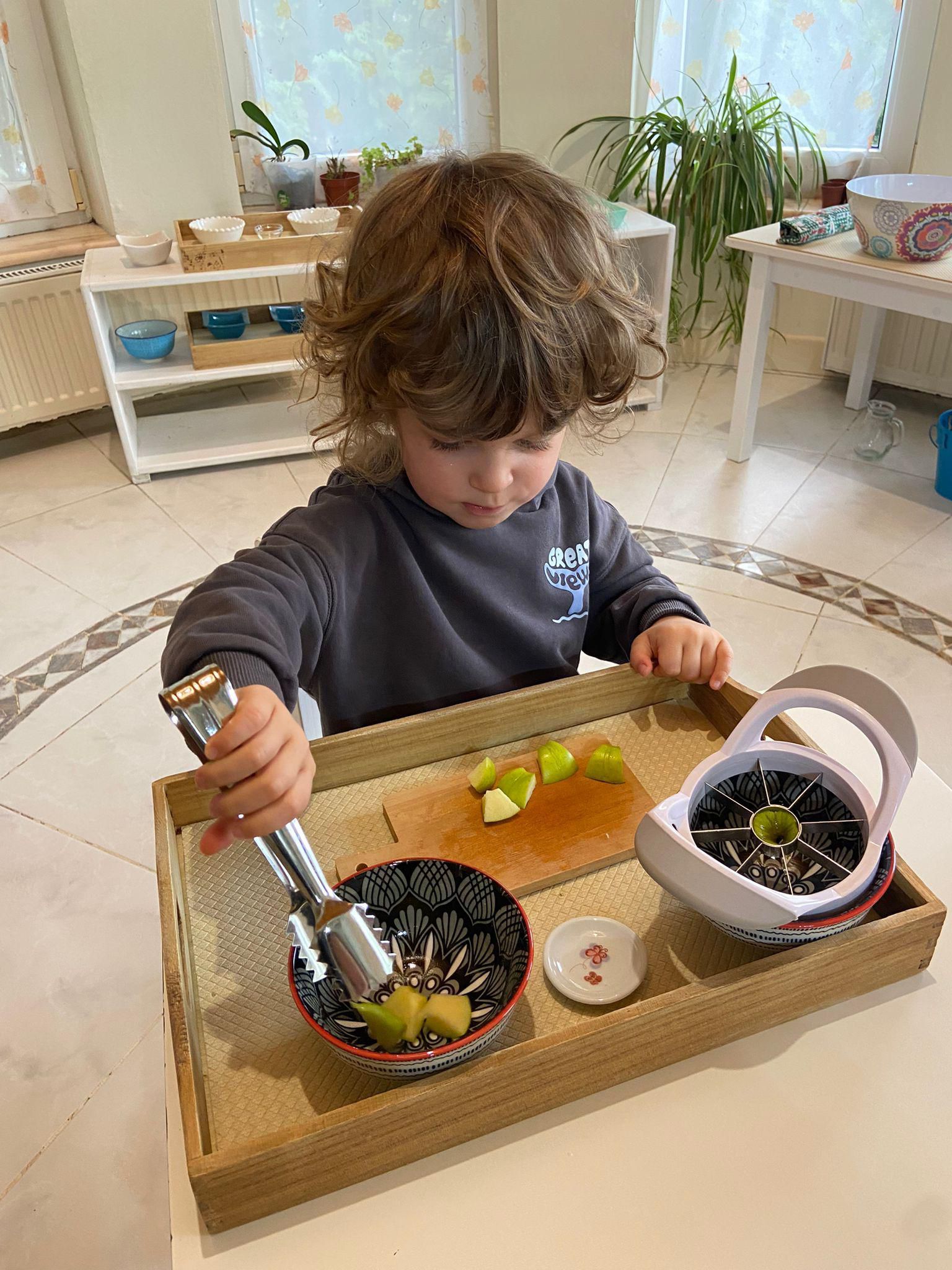 A young boy is sitting at a table playing with a tray of food.