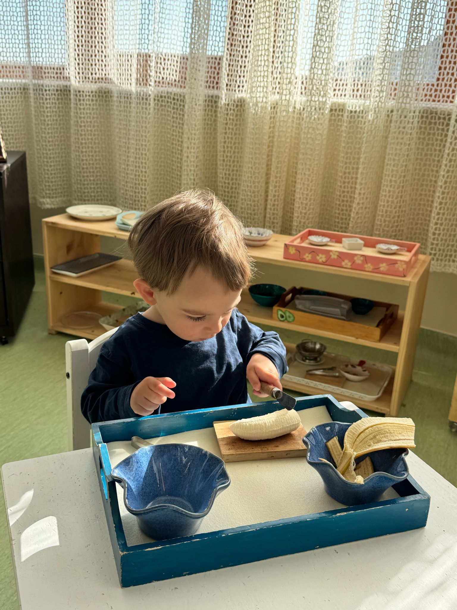 A young boy is sitting at a table playing with a tray of food.