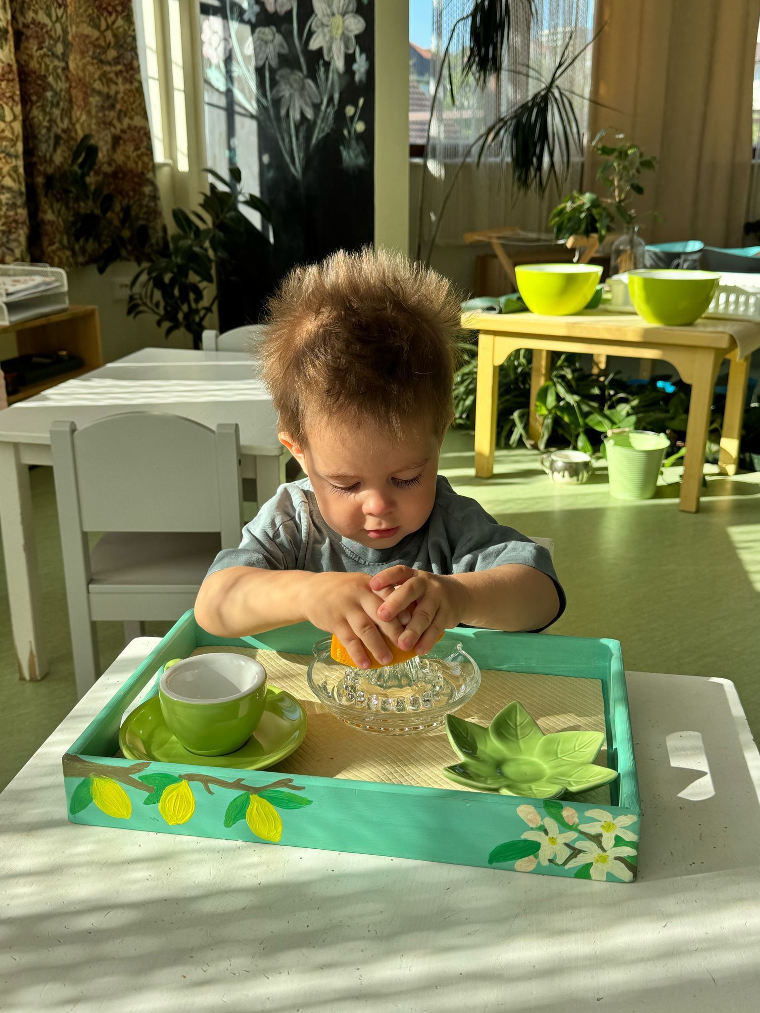 A little boy is sitting at a table playing with an orange.