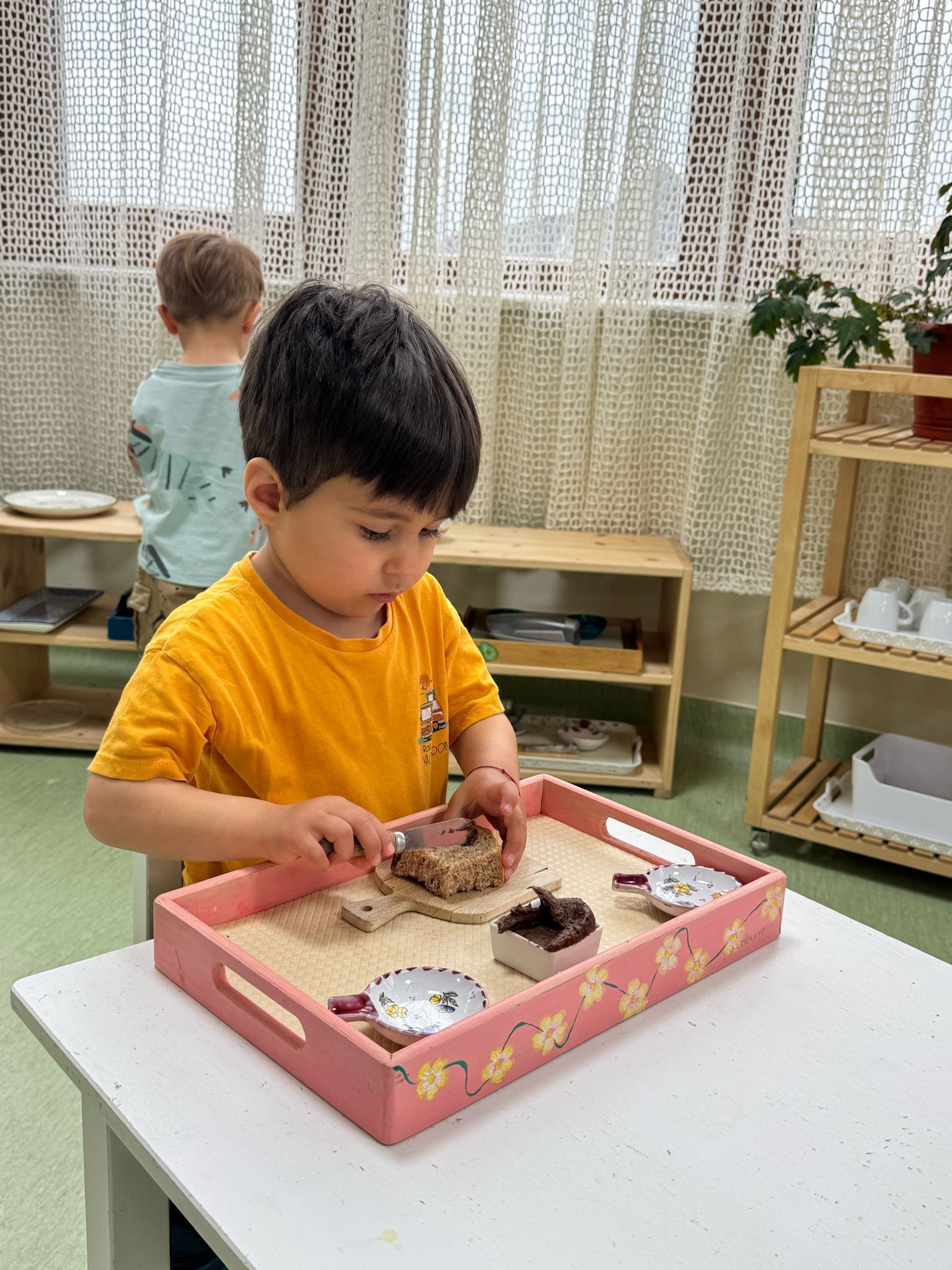 A young boy is playing with a pink tray on a table.