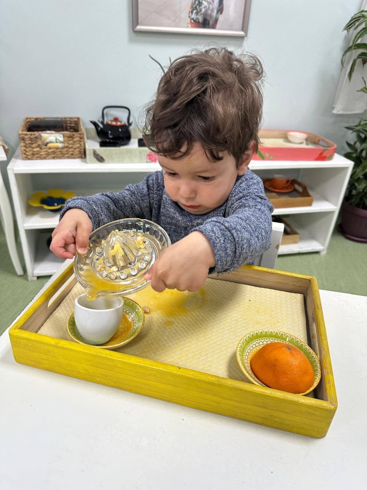A young boy is pouring something into a cup on a tray.