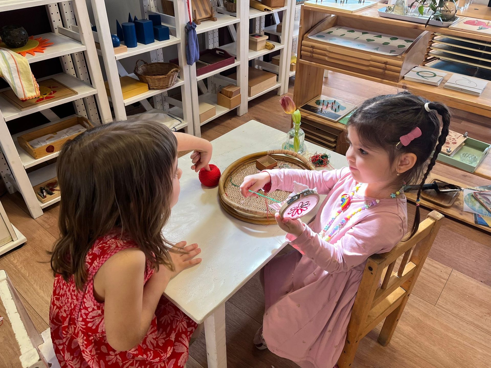 Two little girls are sitting at a table in a classroom playing with apples.