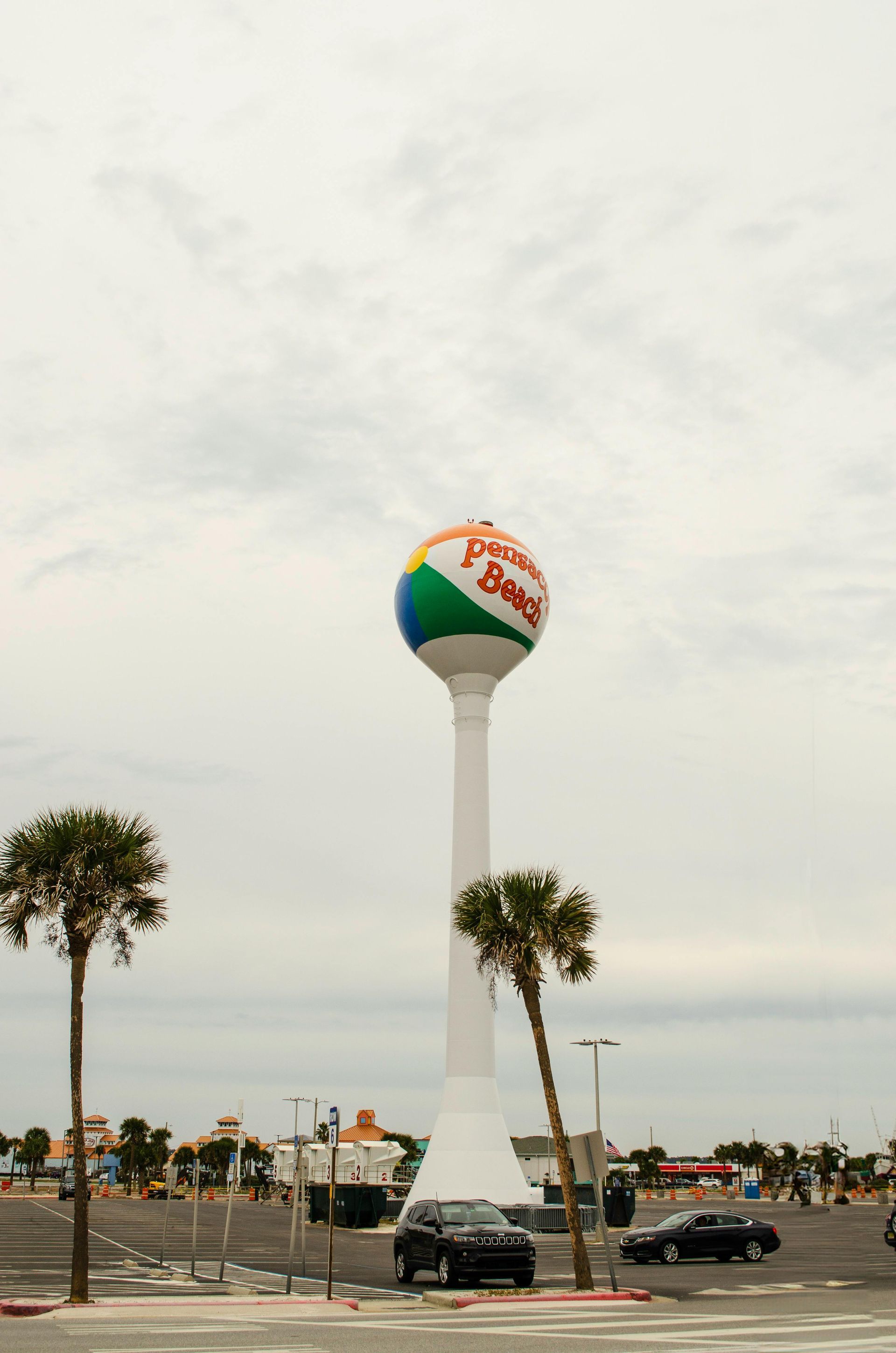 A water tower with a beach ball on it is in a parking lot.
