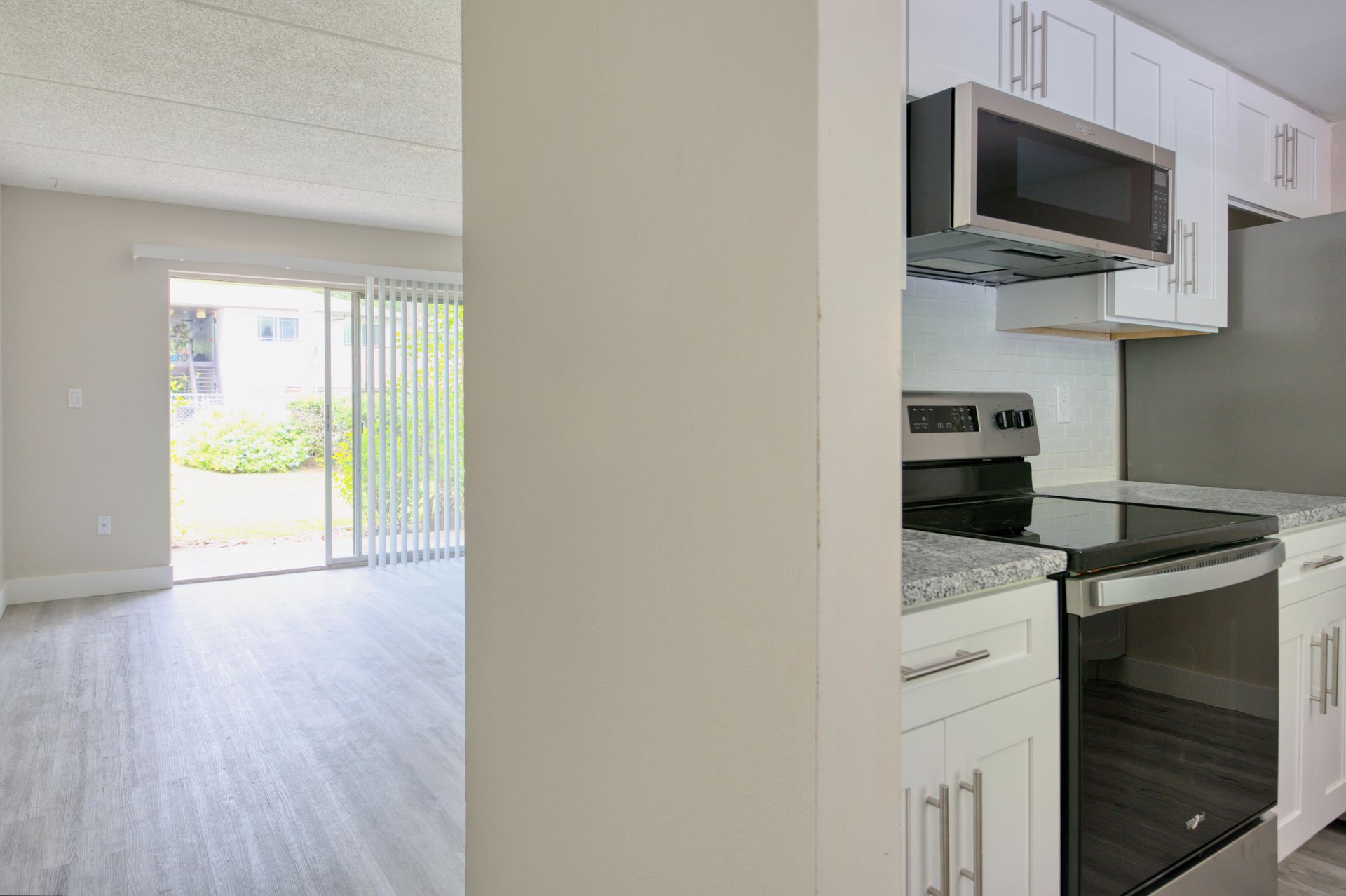 A kitchen and living room with a stove, microwave and sliding glass door.