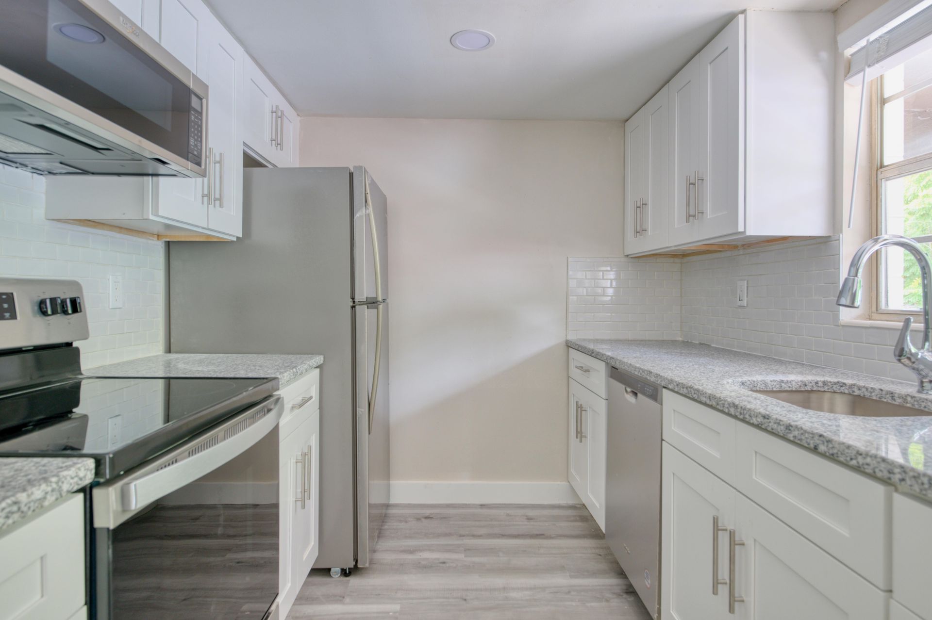 A kitchen with stainless steel appliances , granite counter tops , white cabinets and a refrigerator.