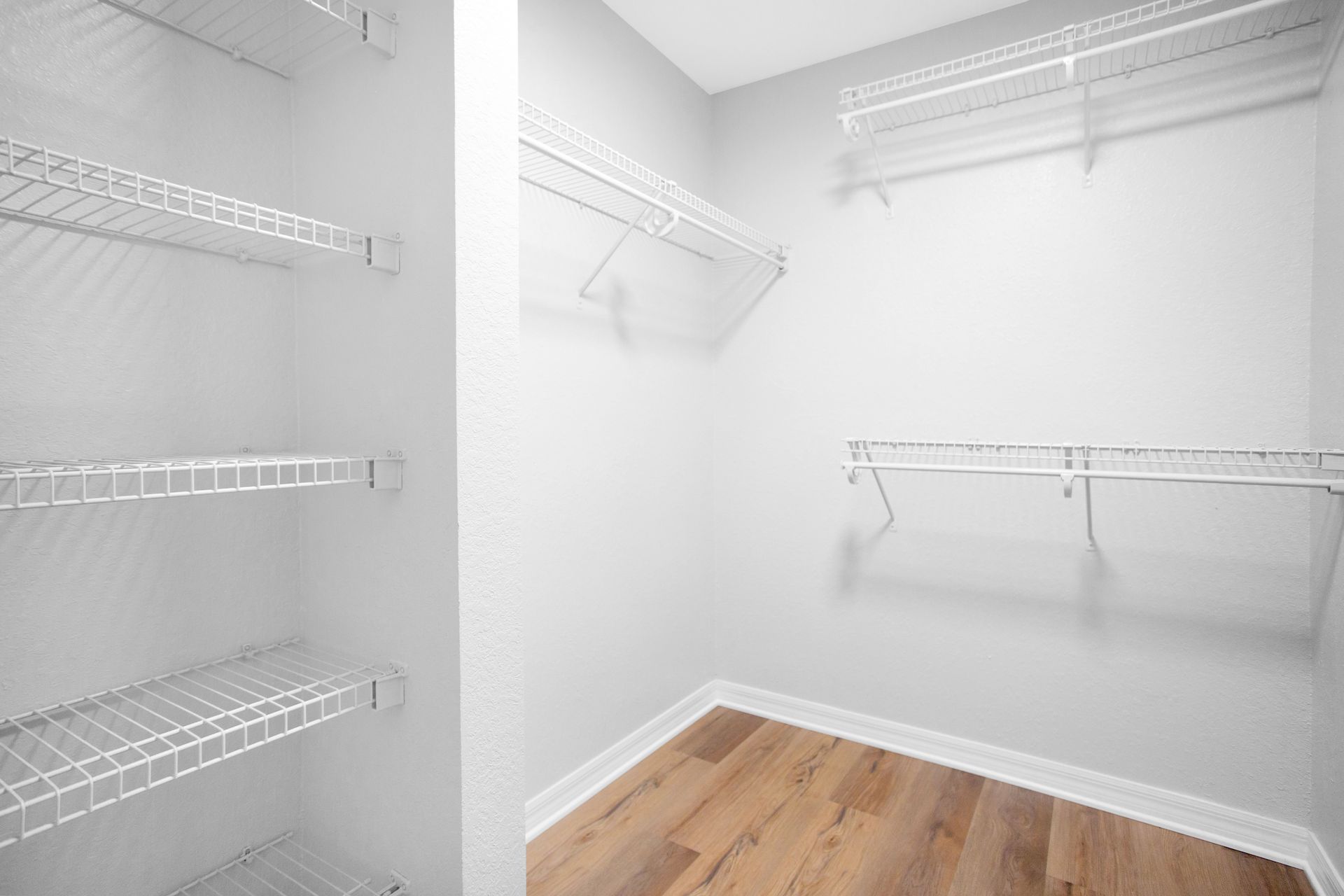 An empty walk in closet with wood vinyl floors and wire shelves.