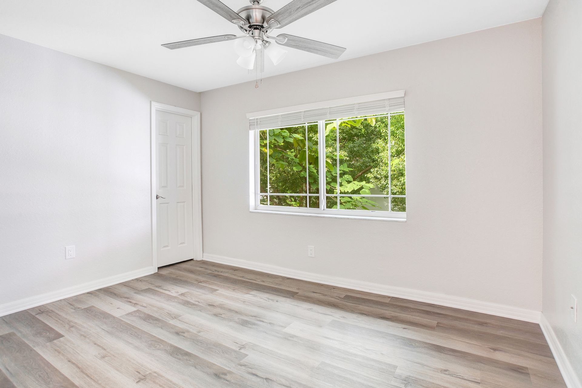 An empty room with a ceiling fan and two windows.