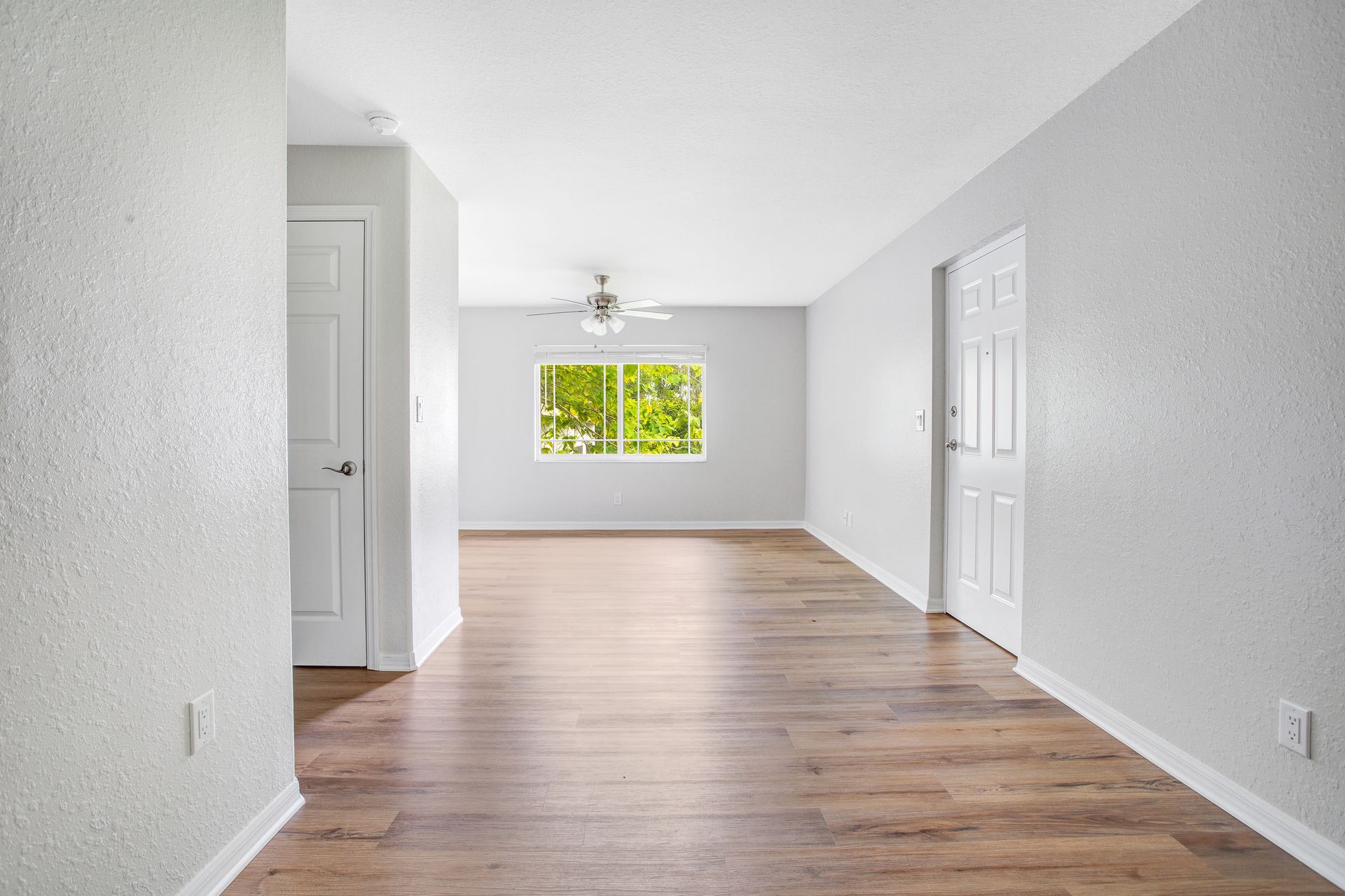 An empty living room with viny floors and a window.