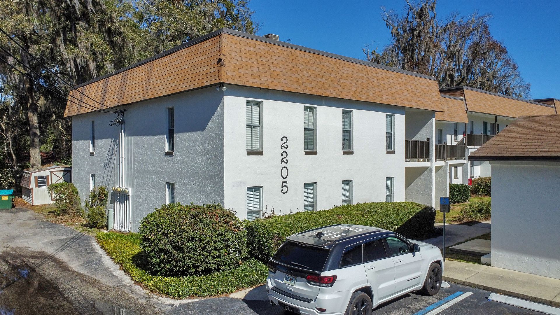 A white apartment building with landscaping and parking in front. 