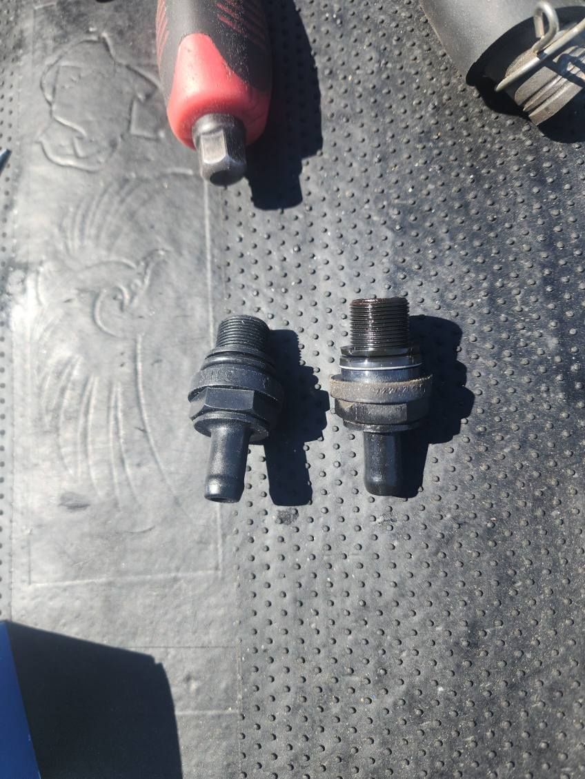 Two screws are sitting on a black surface next to a screwdriver.